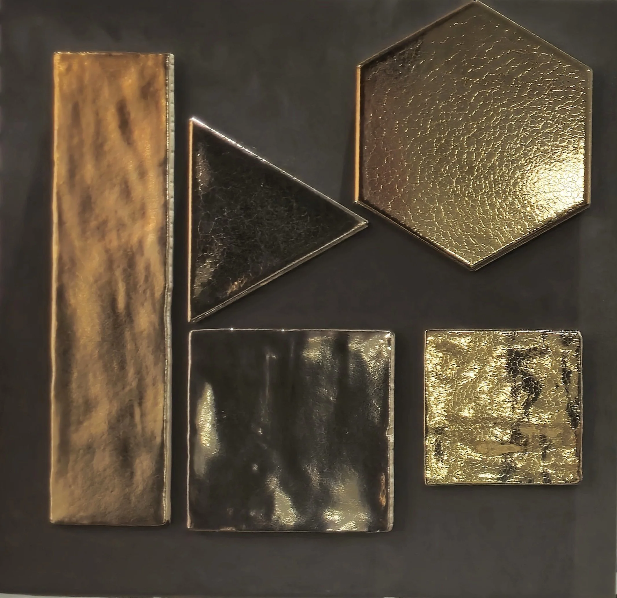 Verschillende geometrische vormen, waaronder een rechthoek, driehoek, zeshoek en vierkanten, van goudkleurig en glanzend materiaal op een donkere achtergrond.