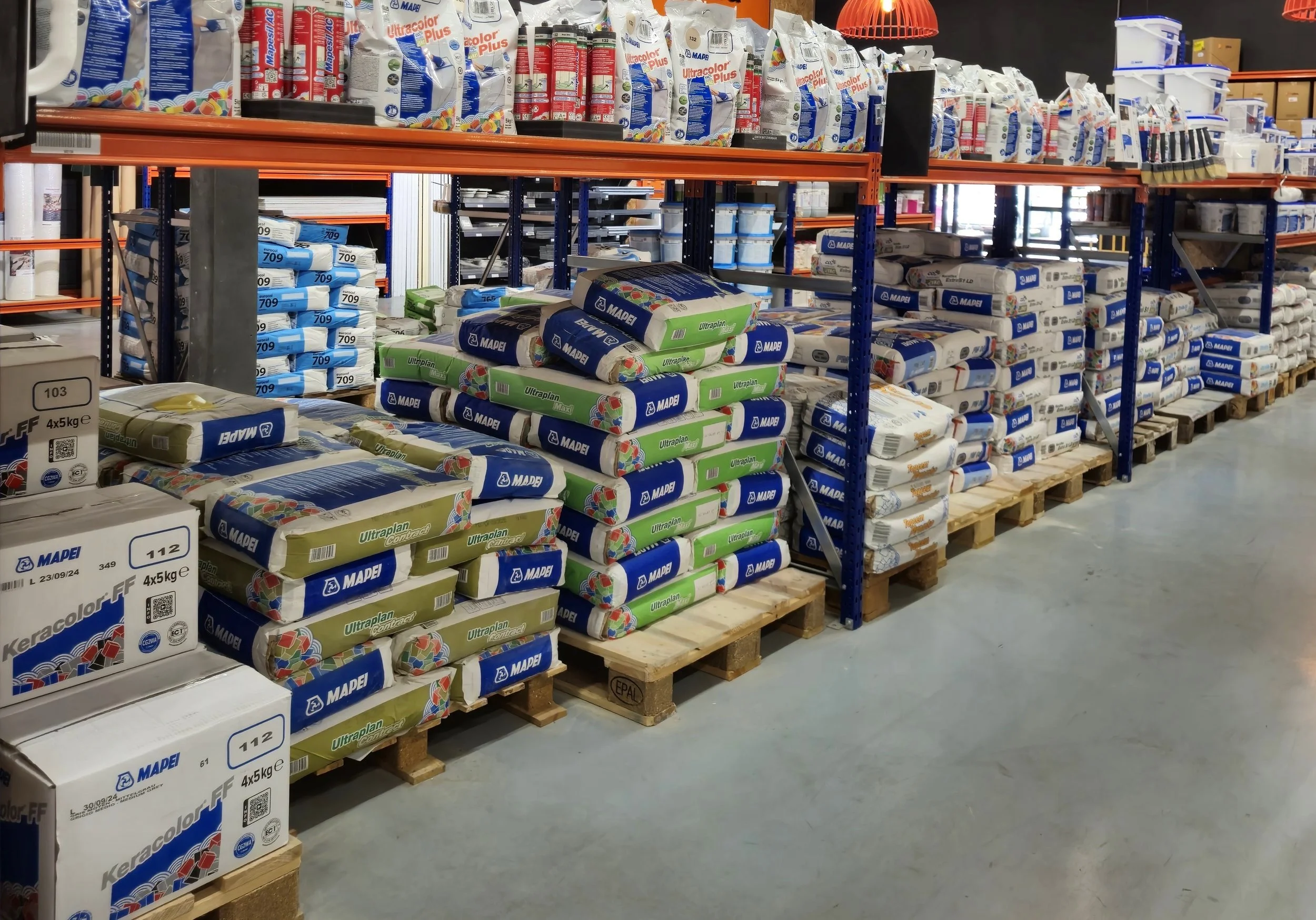 Stellingen met gestapelde zakken en dozen bouwmaterialen in een magazijn.