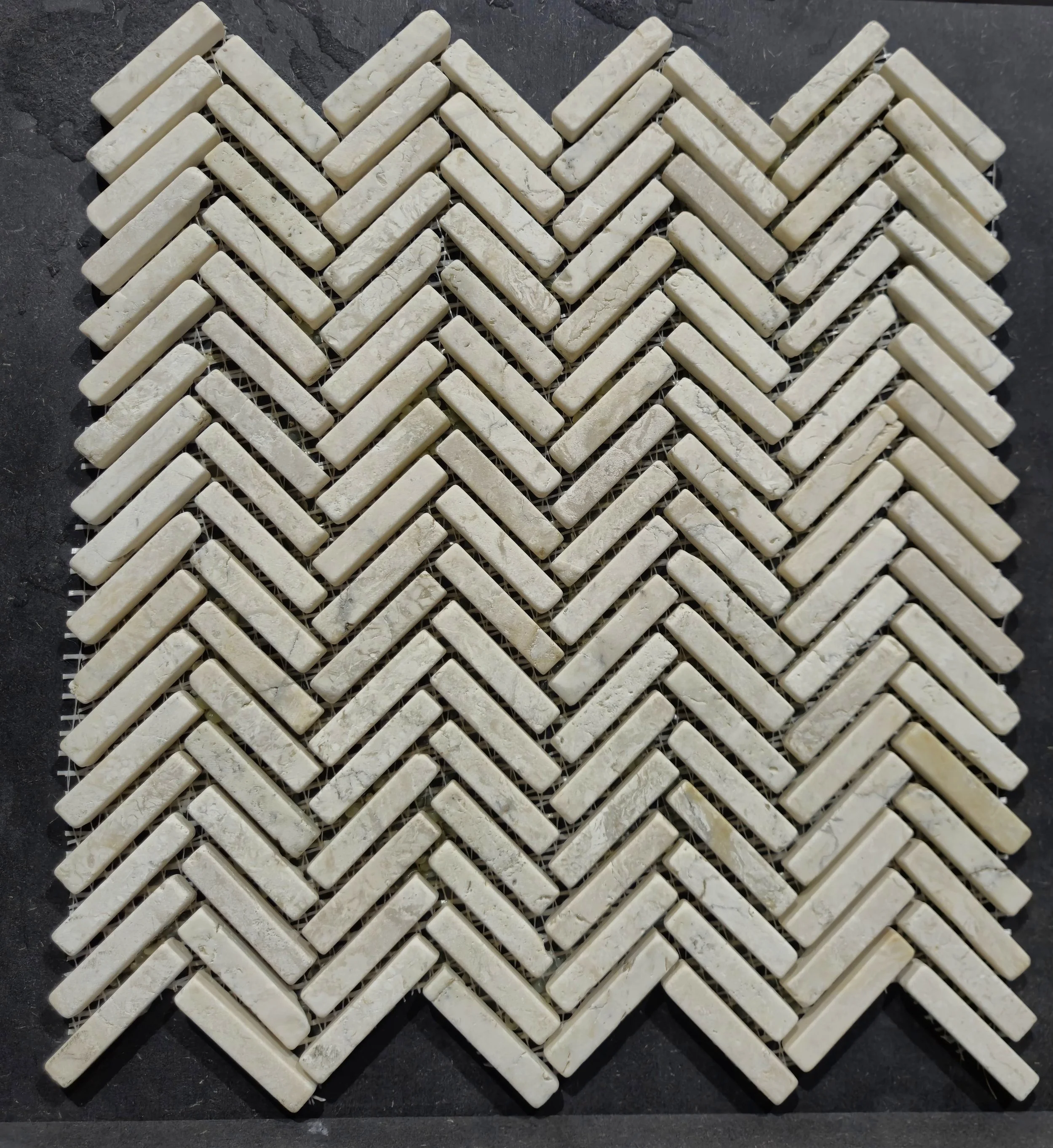 Visgraatpatroon van lichte stenen tegels op een donkere achtergrond.