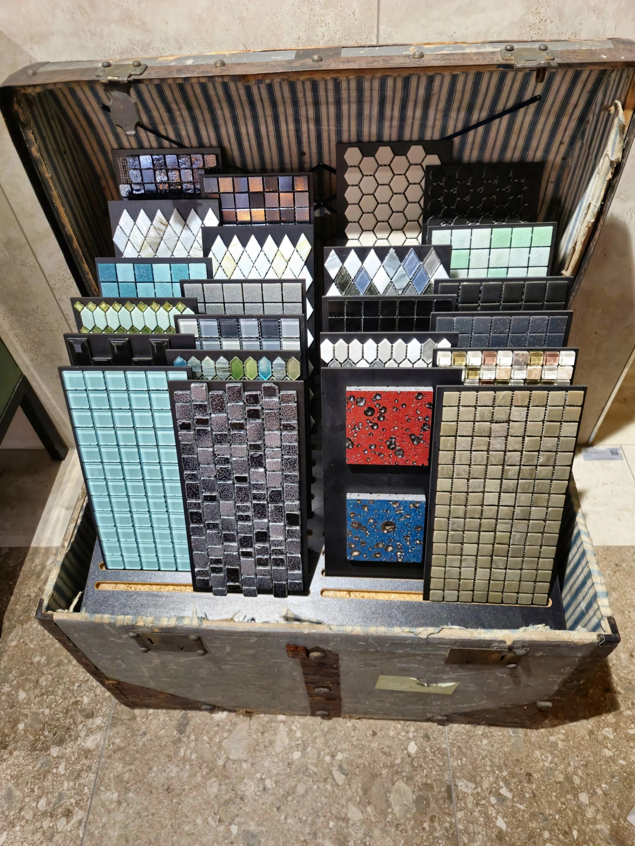 Diverse mozaïektegelmonsters in een open koffer op de vloer.