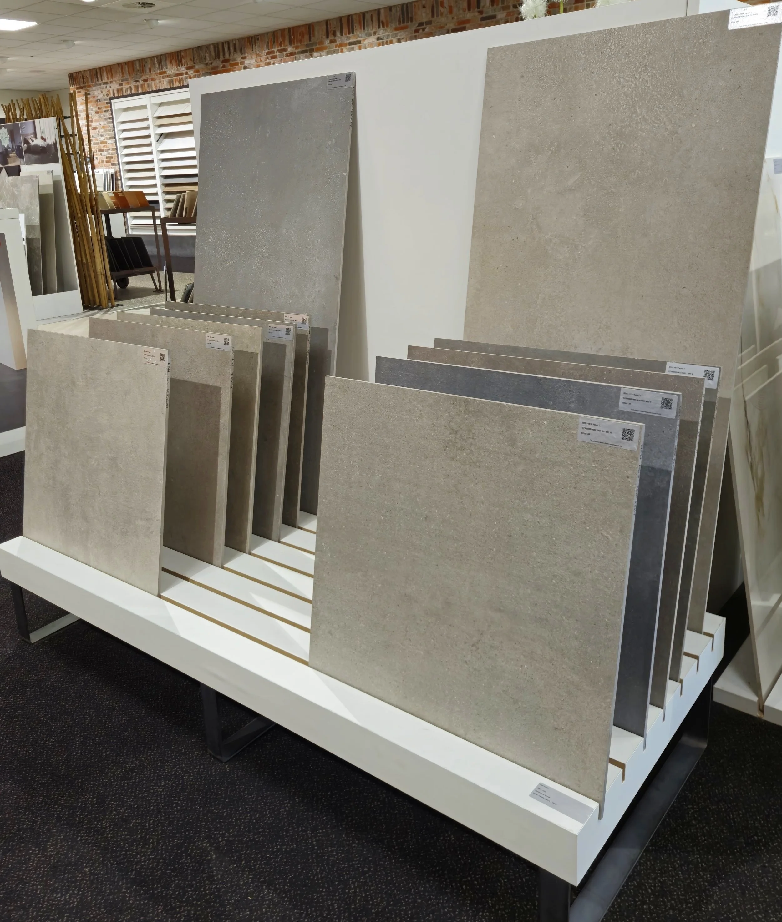 Tegels in verschillende maten en kleuren gepresenteerd in een showroom, geplaatst op een witte standaard.