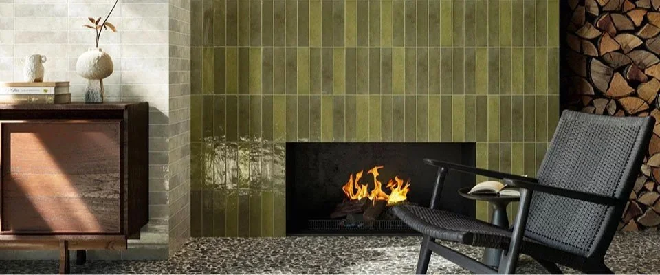 Interieur met open haard, groene tegels, zwarte stoel, houten kastje, en houtblokken.