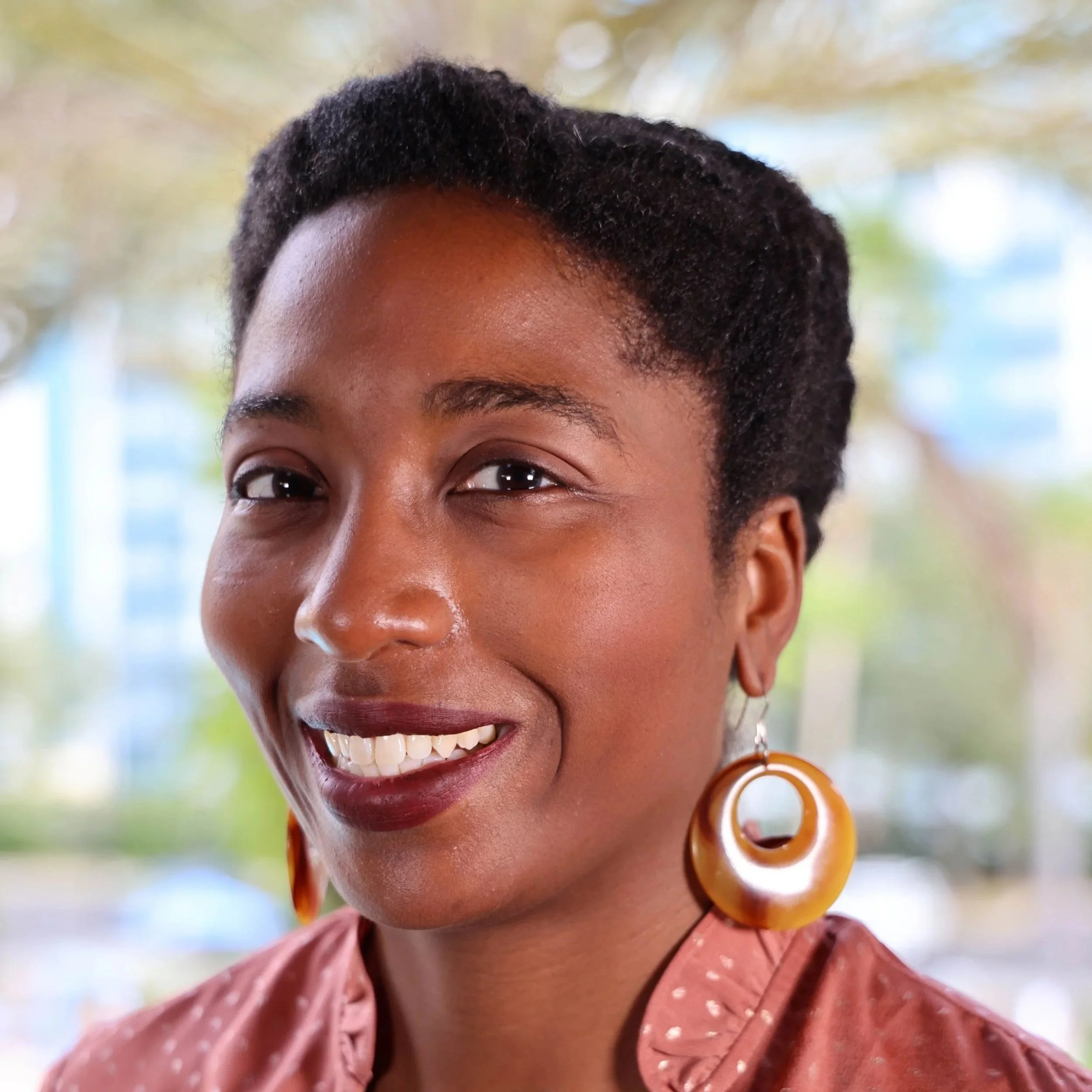 headshot of lowercase legal member Andrea Lowe black woman wearing gold hoop earrings and blush blouse