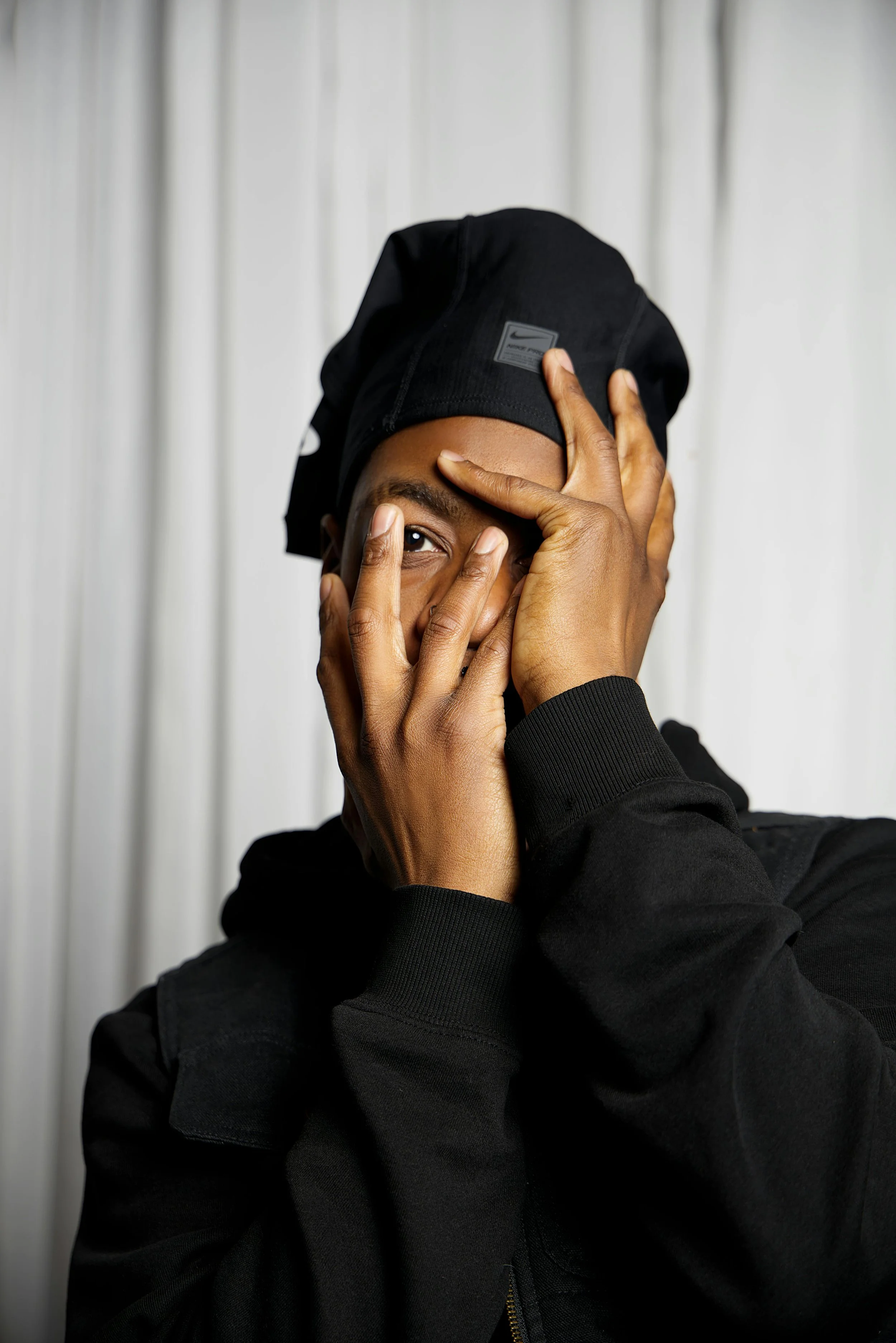 black man black hat black sweatshirt hands covering face