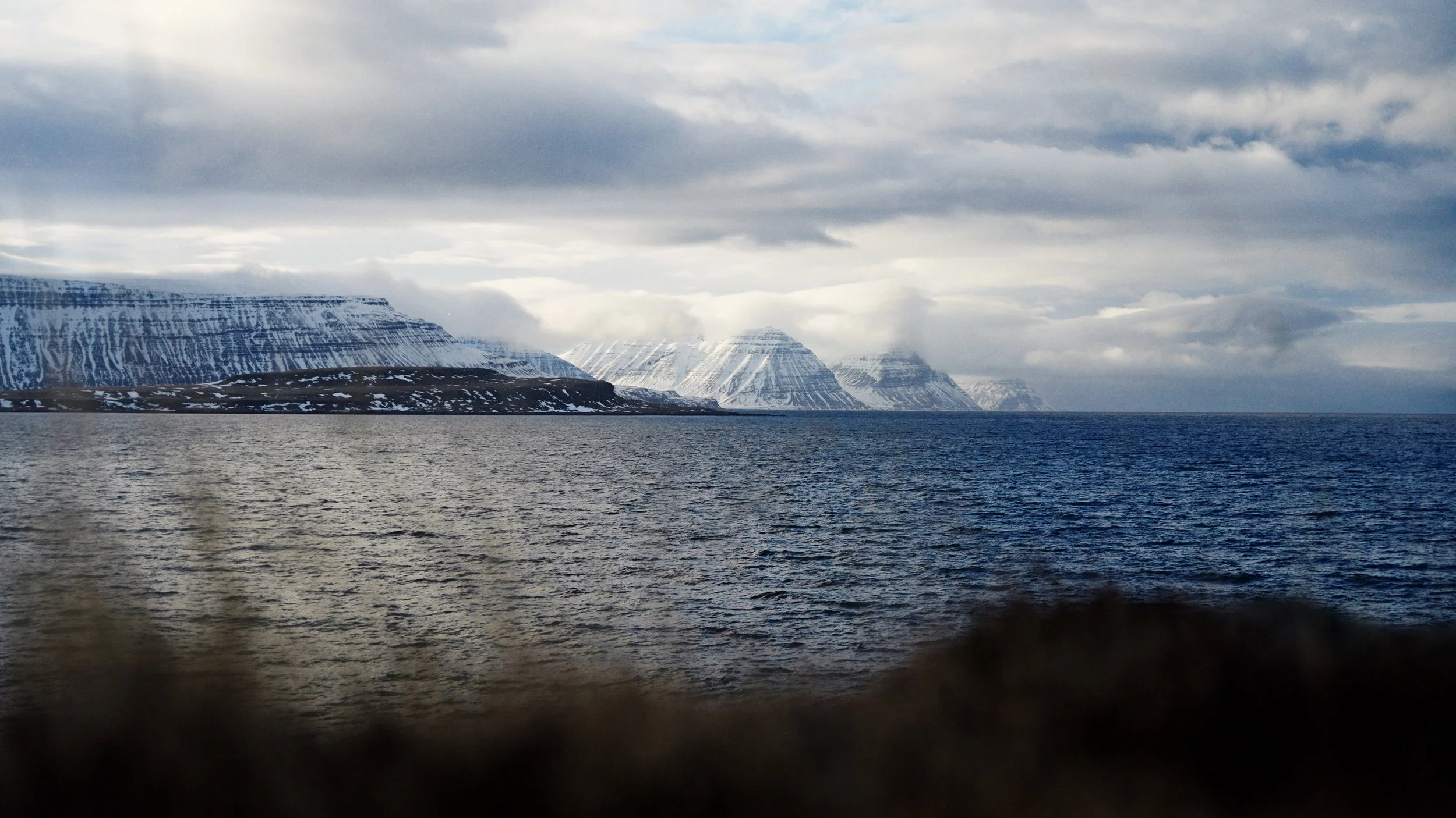 Snow-covered mountains meeting the ocean under cloudy skies.