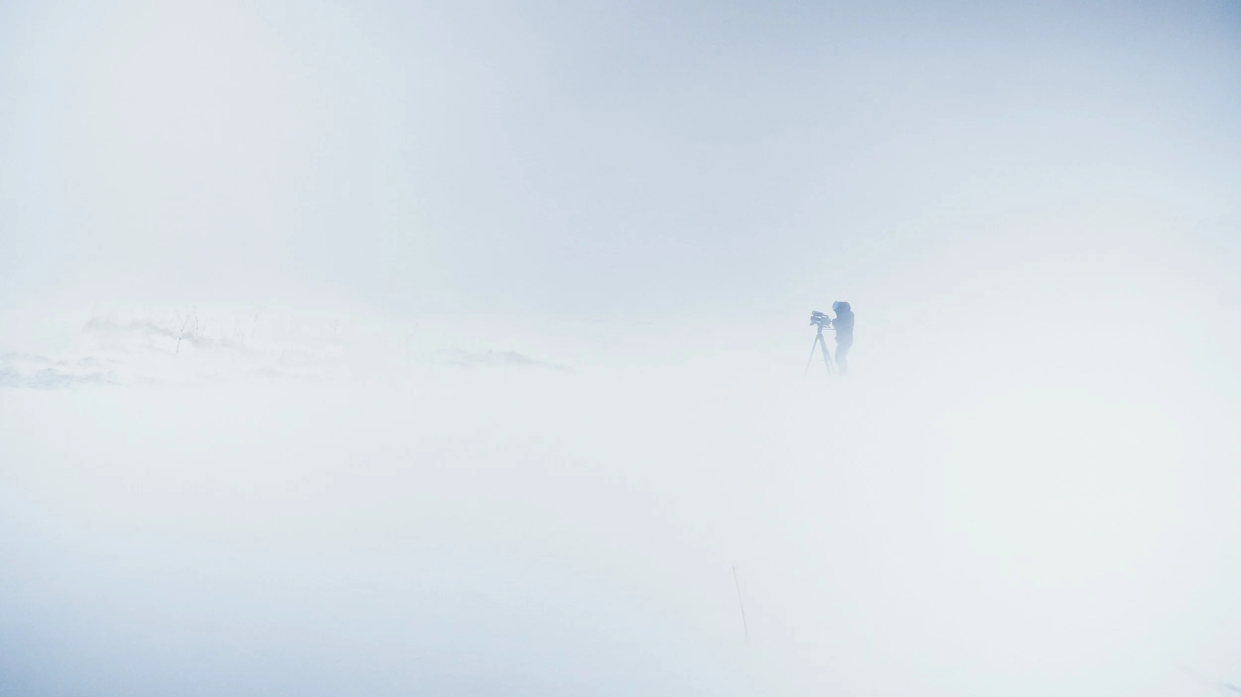 A photographer setting up a camera on a tripod in a foggy, snow-covered landscape.