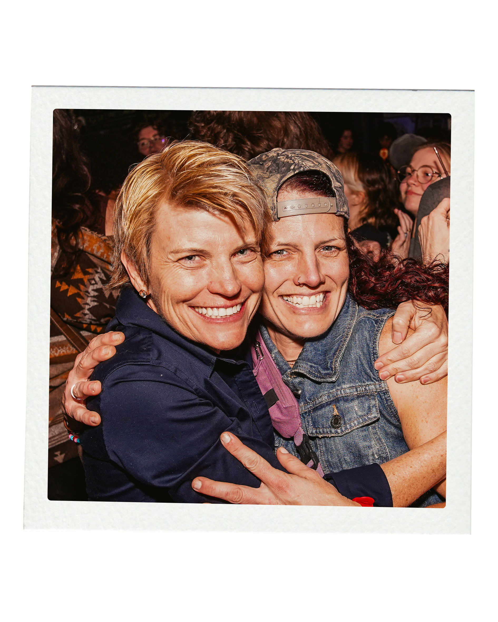 Two women hugging and smiling at a crowded event.