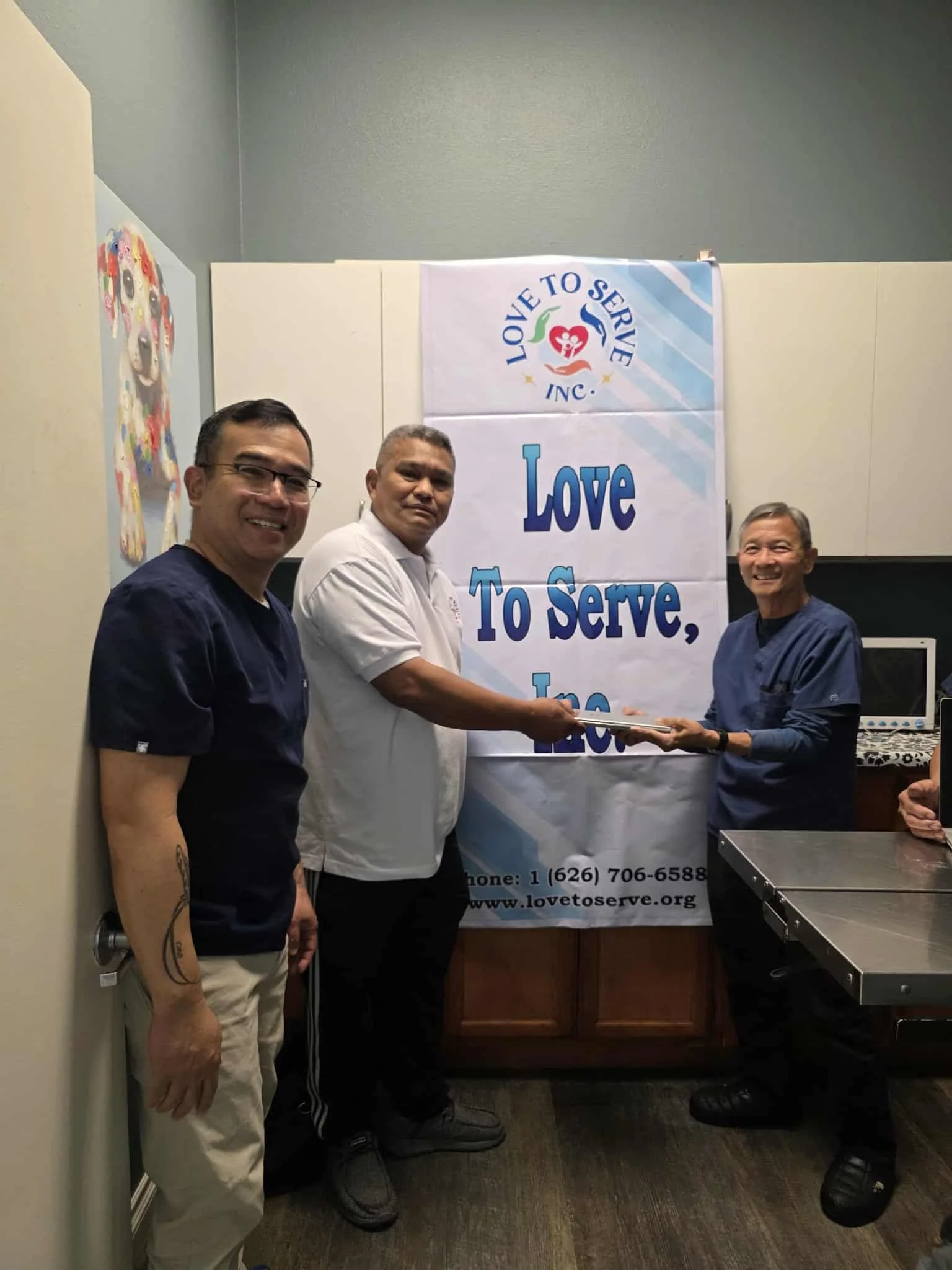 Three men standing in front of a banner that reads "Love to Serve, Inc." at a community event, one man is handing a document or certificate to another.