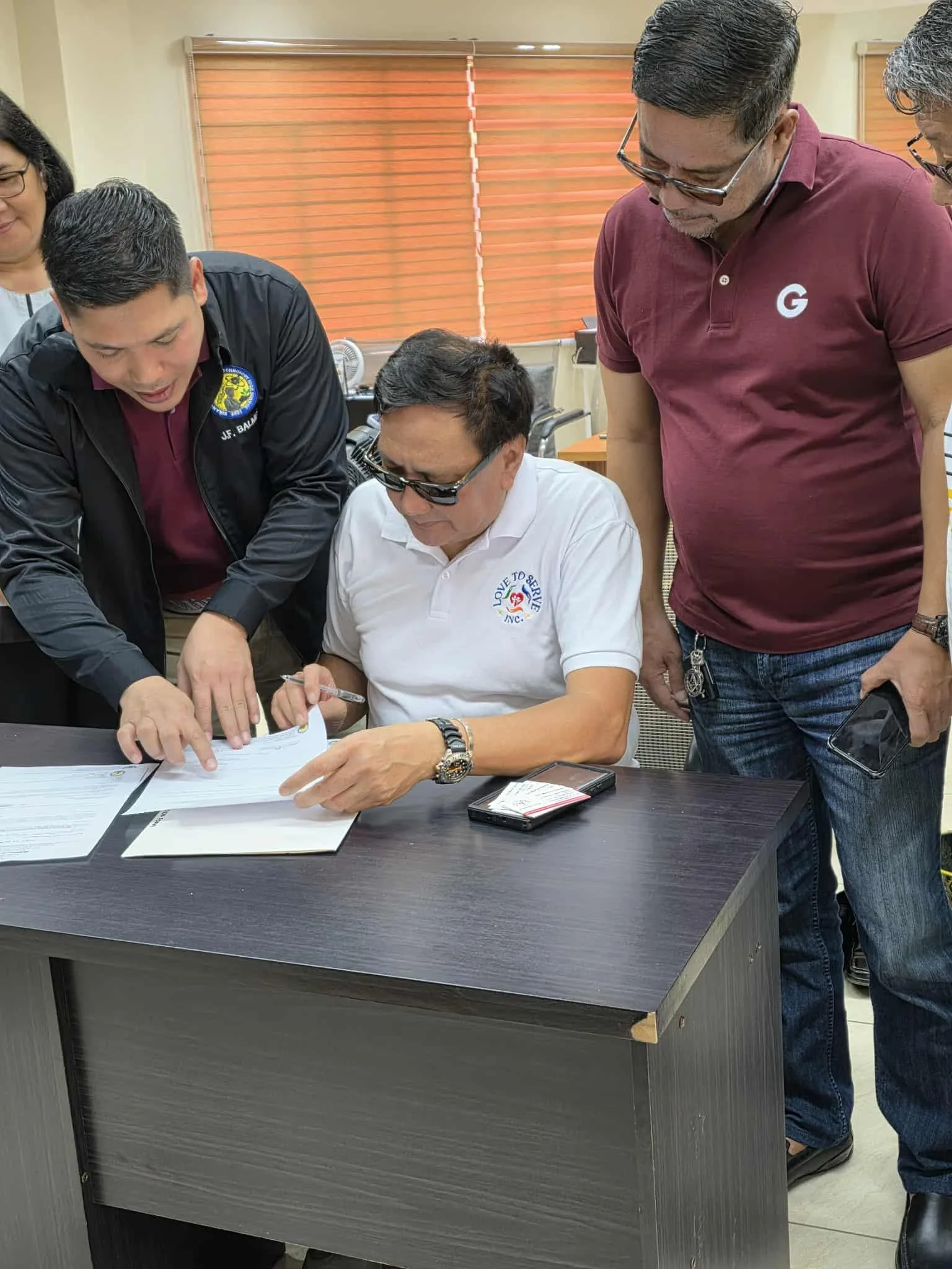 Men gathered around a table reviewing documents in an indoor office setting.