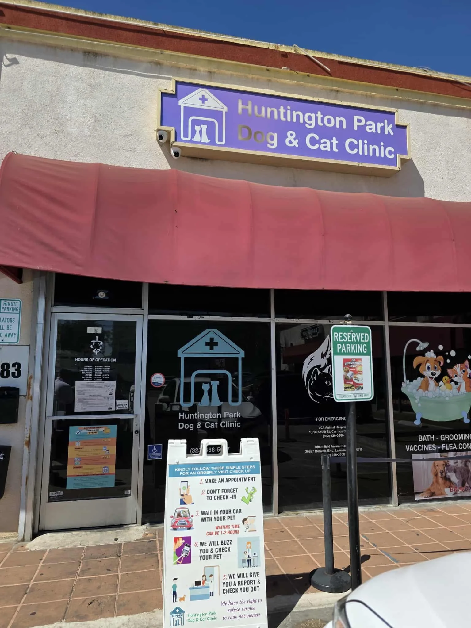 The image shows the exterior of Huntington Park Dog & Cat Clinic with signage displayed above the entrance and a detailed step-by-step appointment procedure sign on the door. There are reserved parking signs and window graphics featuring cartoon anim