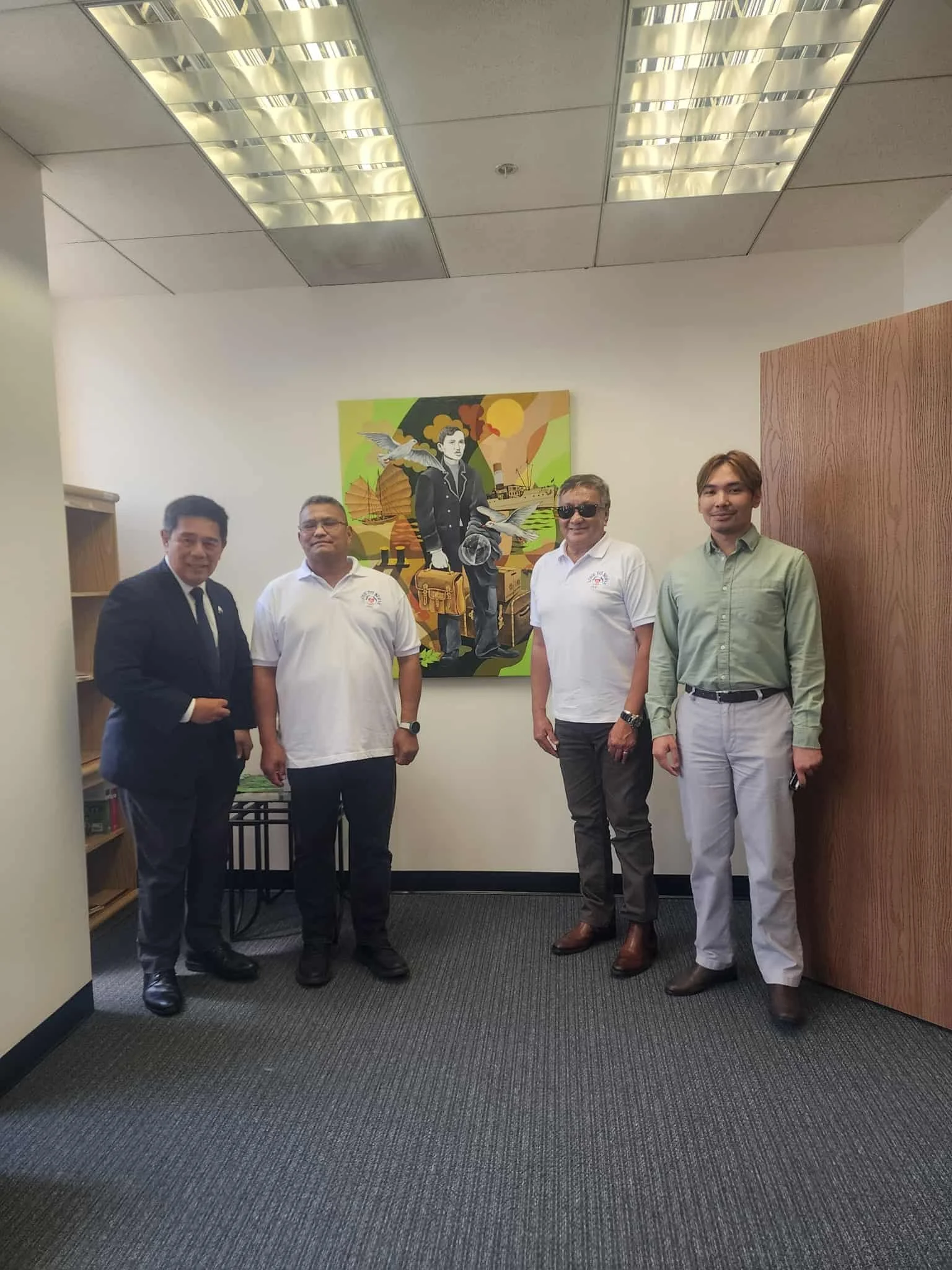 Five men standing in a room with a colorful painting of a woman and birds behind them.