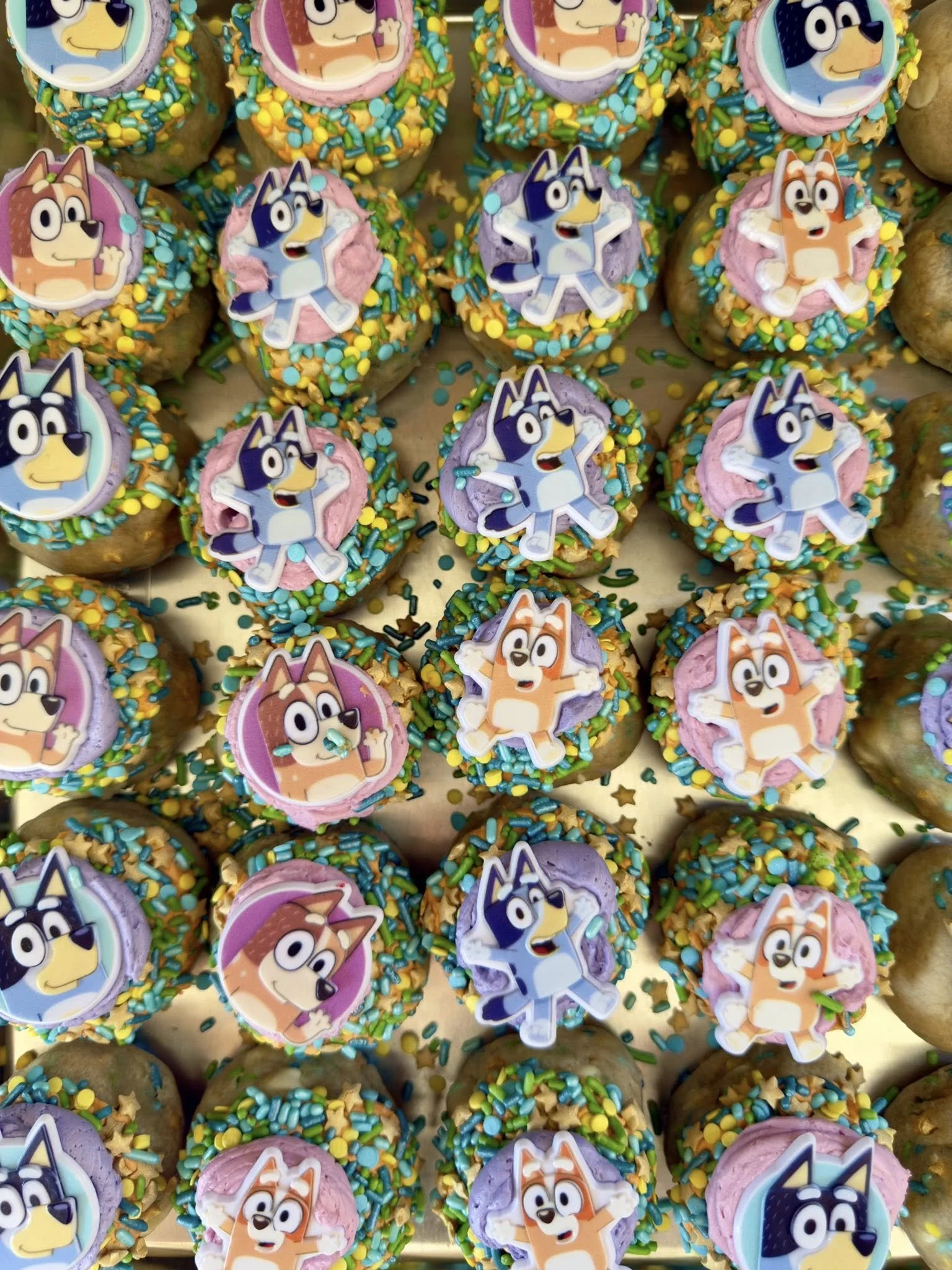 Colorful cookies decorated with character toppers from an animated series, with sprinkles and frosting in pastel colors.