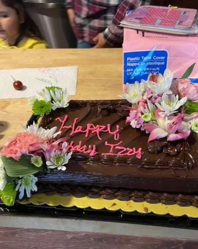 Chocolate birthday cake decorated with pink and white flowers, with pink icing writing that says "Happy Birthday Izzy".
