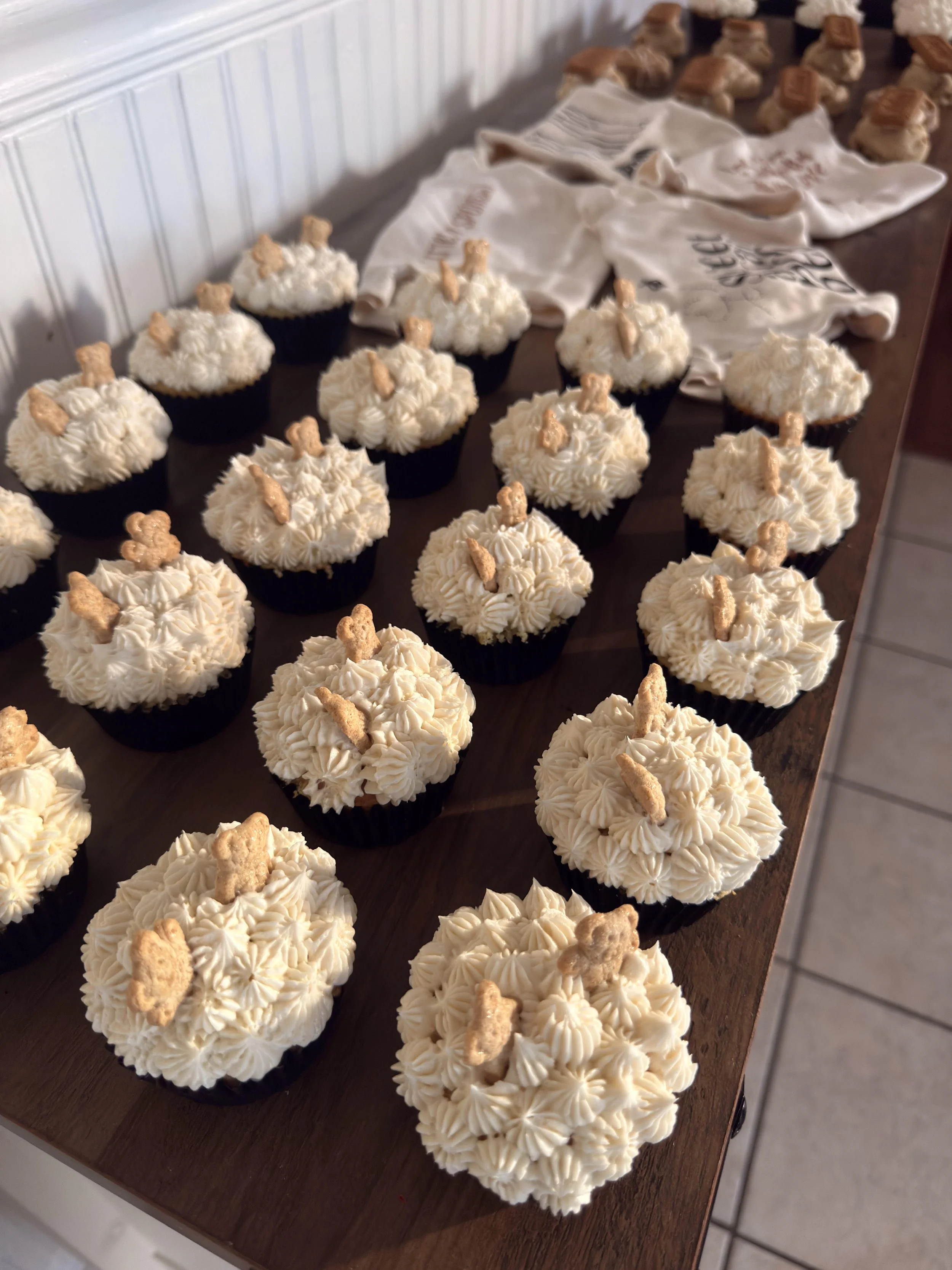 Cupcakes topped with white frosting and small teddy bear-shaped cookies on a wooden table.