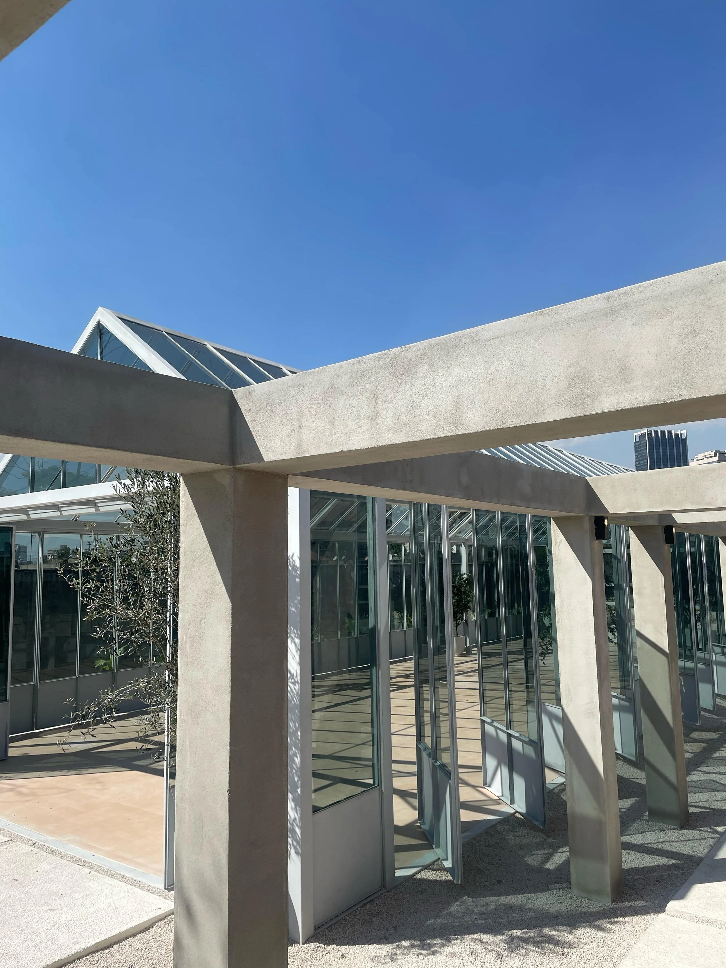 Modern building with glass walls and concrete beams, bright sunny day, blue sky.