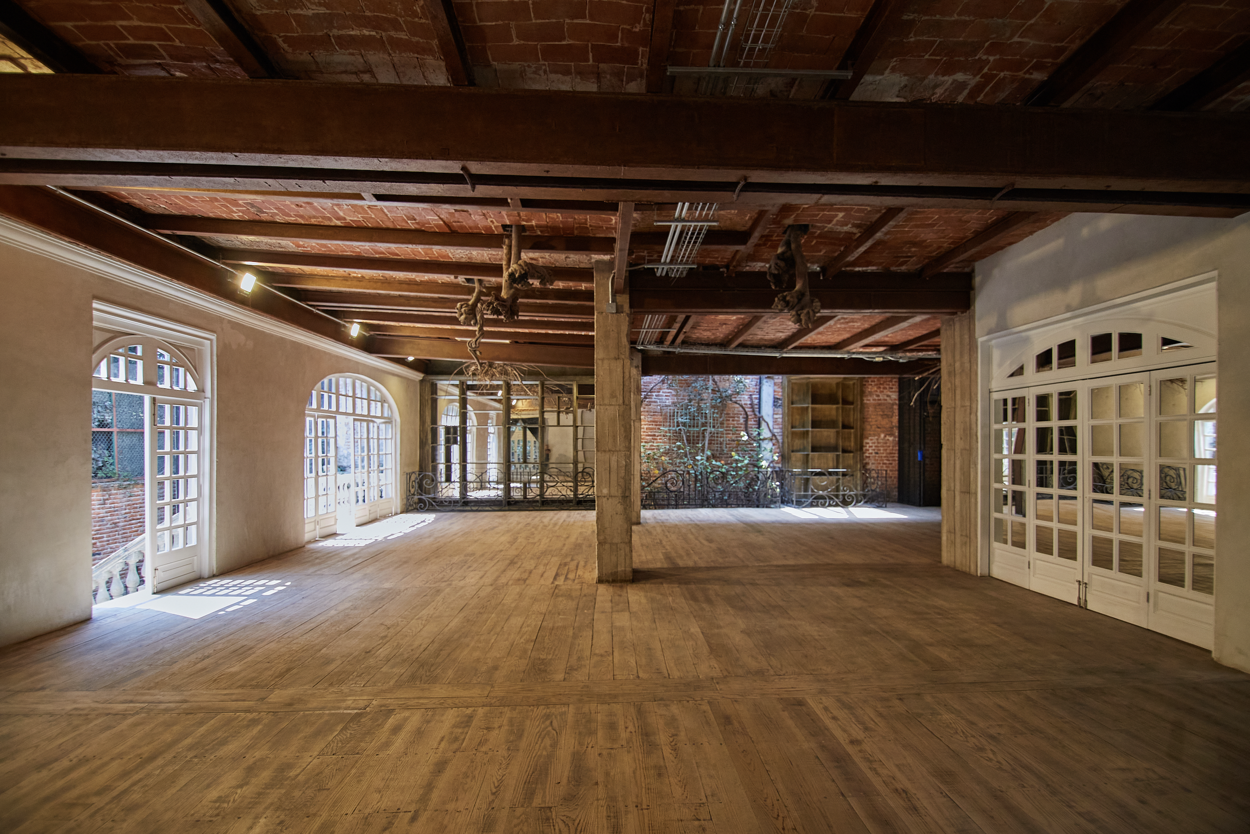 Empty spacious room with wooden floors, large windows, brick walls, and an exposed brick ceiling with wooden beams.