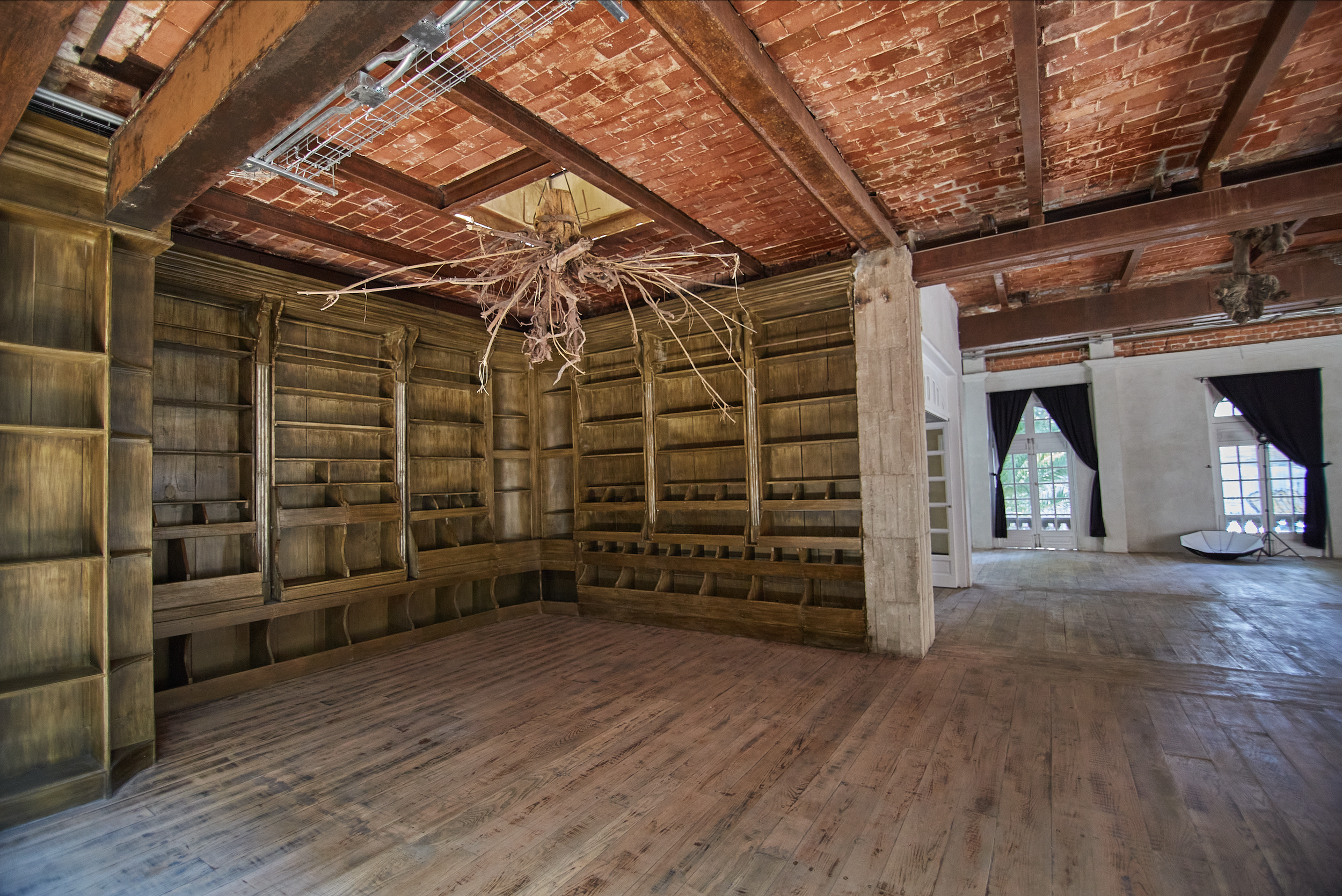 Interior of a room with wooden bookshelves and a brick ceiling, with an open space and large windows with black curtains.