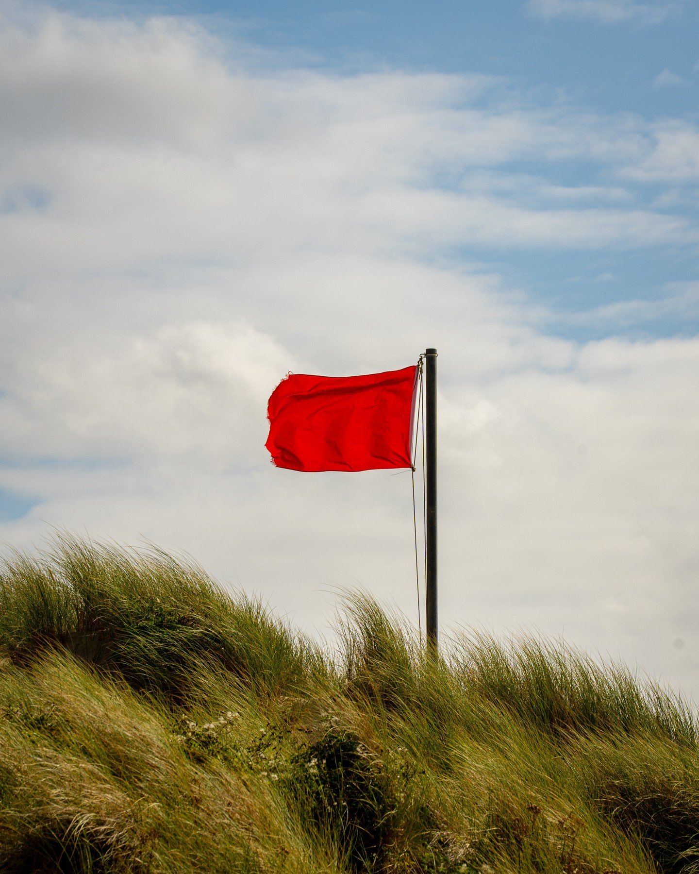 A stark red flag on the dunes above Abermawr, held between warning, marker and signal.

Against the open coast, a small vertical interruption reorganises the field around it.

#ContemporaryArt #LandscapePhotography #Abermawr #Signal #StephenWadcock