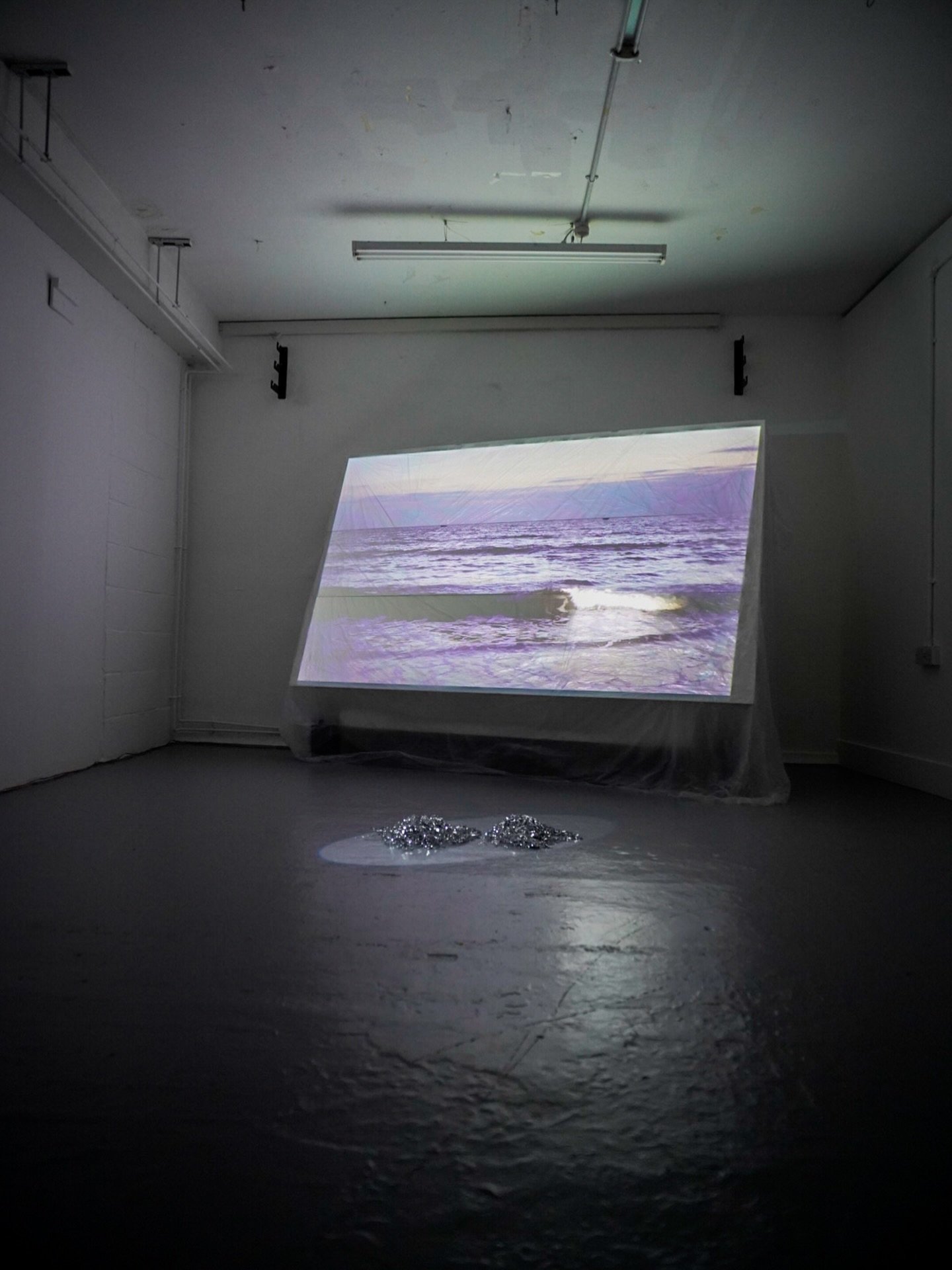 What Passes for the Sea, 2026
Sculptural installation, projected moving image, sound, transparent polyethylene sheeting, tinsel pom-poms and light.
Approx. 240 &times; 200 &times; 100 cm (W &times; H &times; D). Eight-minute video loop.

#fineart #sc