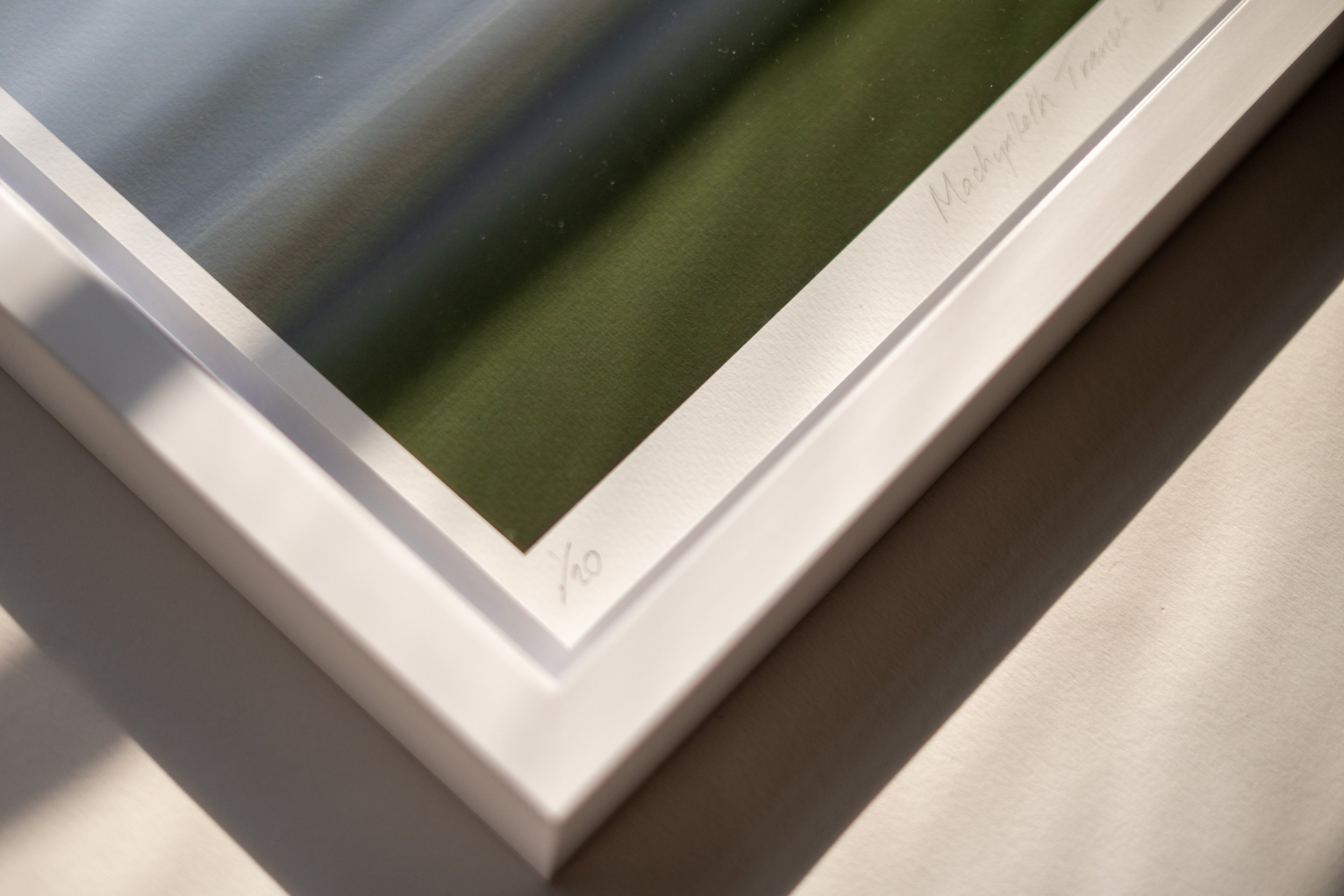 Close-up of a framed artwork or print with a handwritten signature or note in the bottom right corner and a white border.