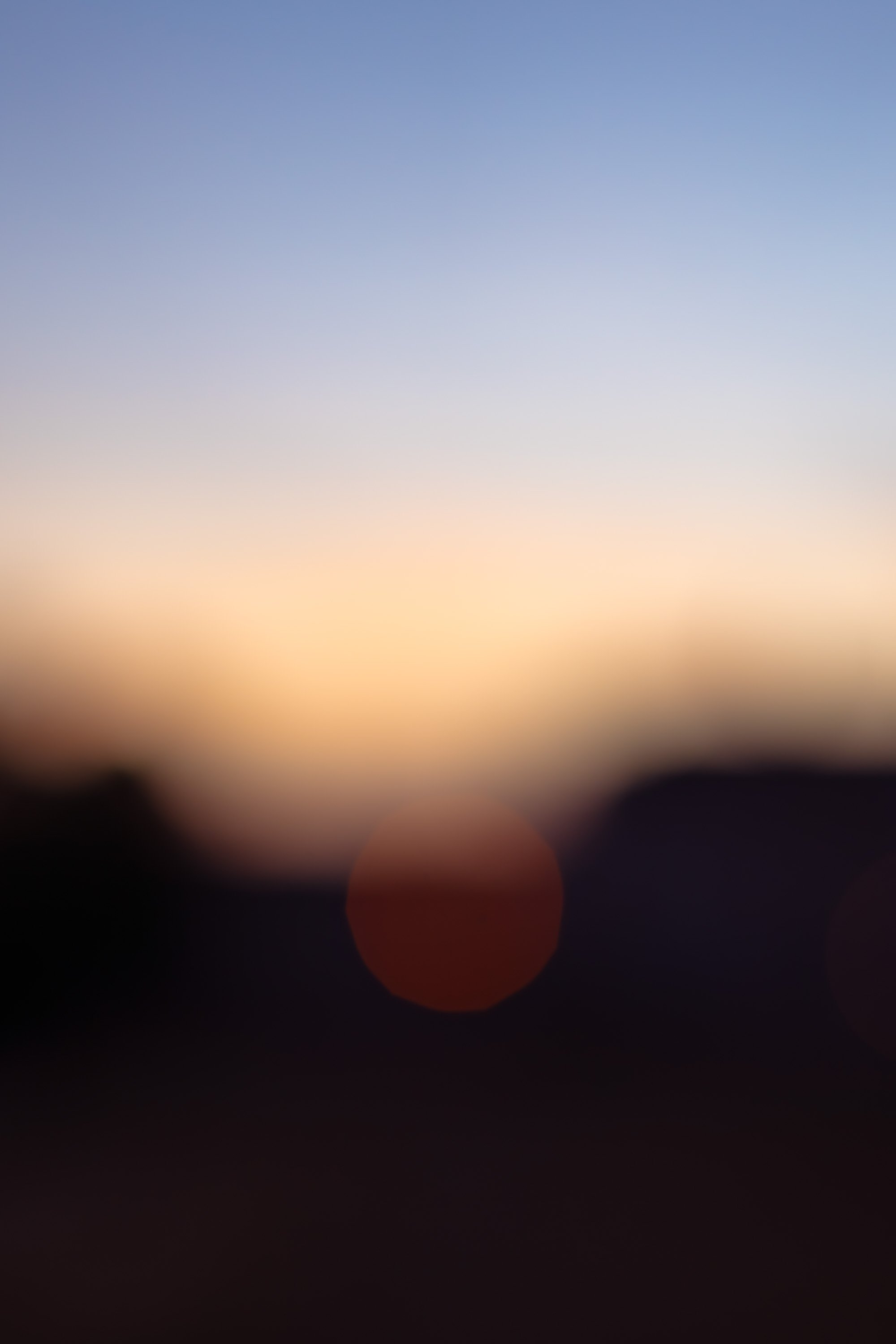 Blurred image of a sunset or sunrise sky with soft gradient colors and bokeh light effects.