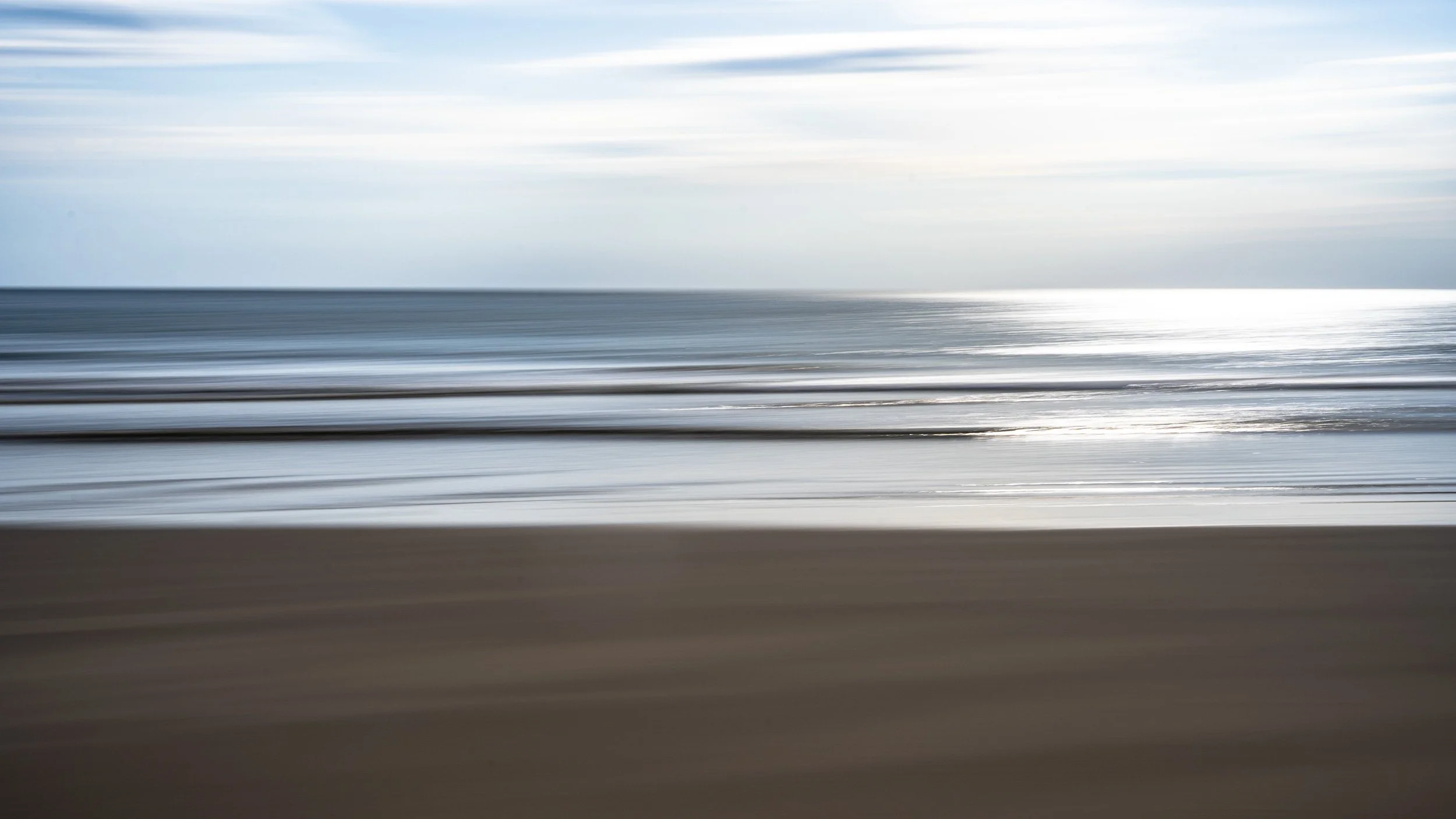 Blurred motion photograph of a beach with waves and the ocean under an partly cloudy sky.