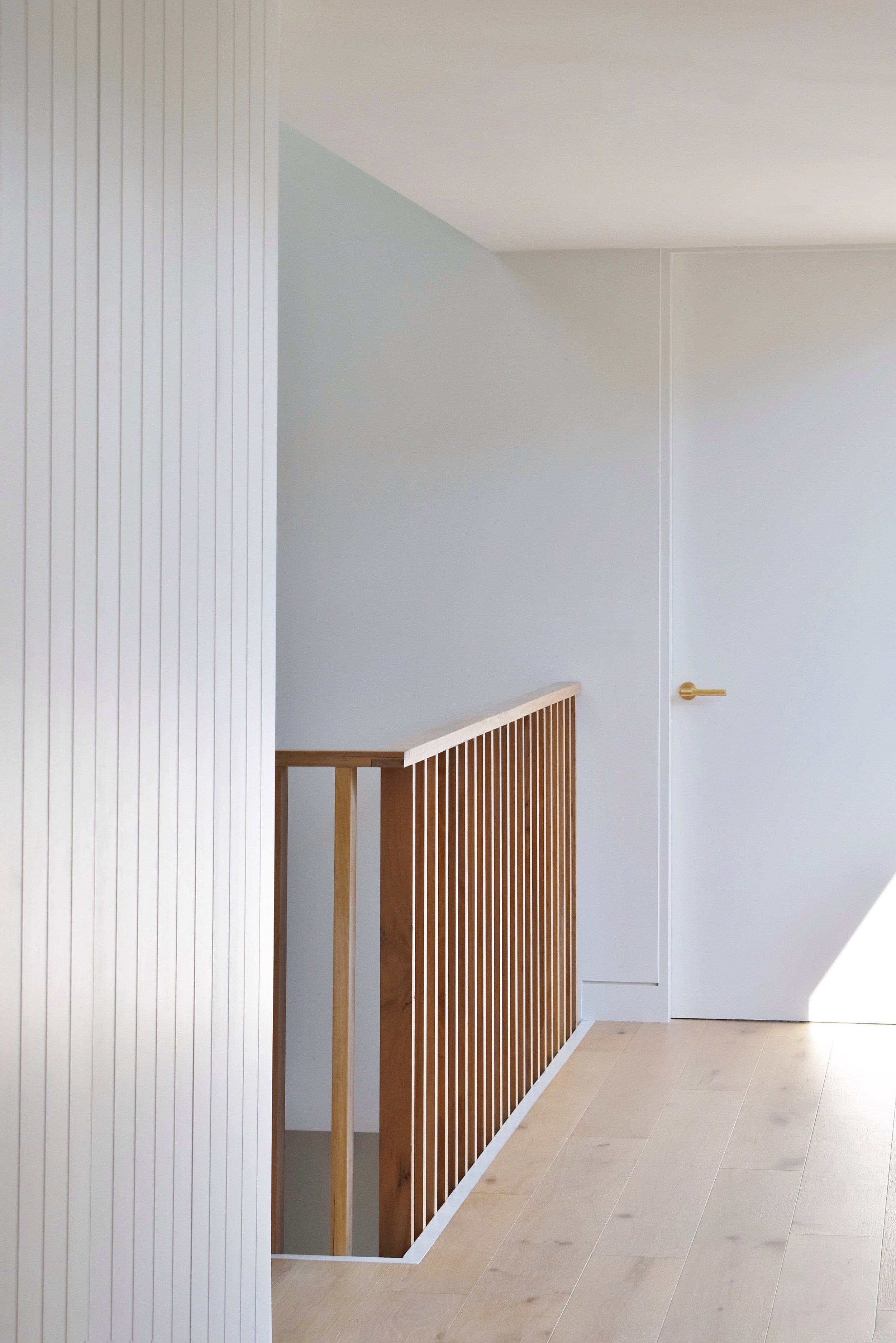 Interior view of the entry hallway with timber balustrade, warm white walls, and a door with a brass handle at the end of the hallway.