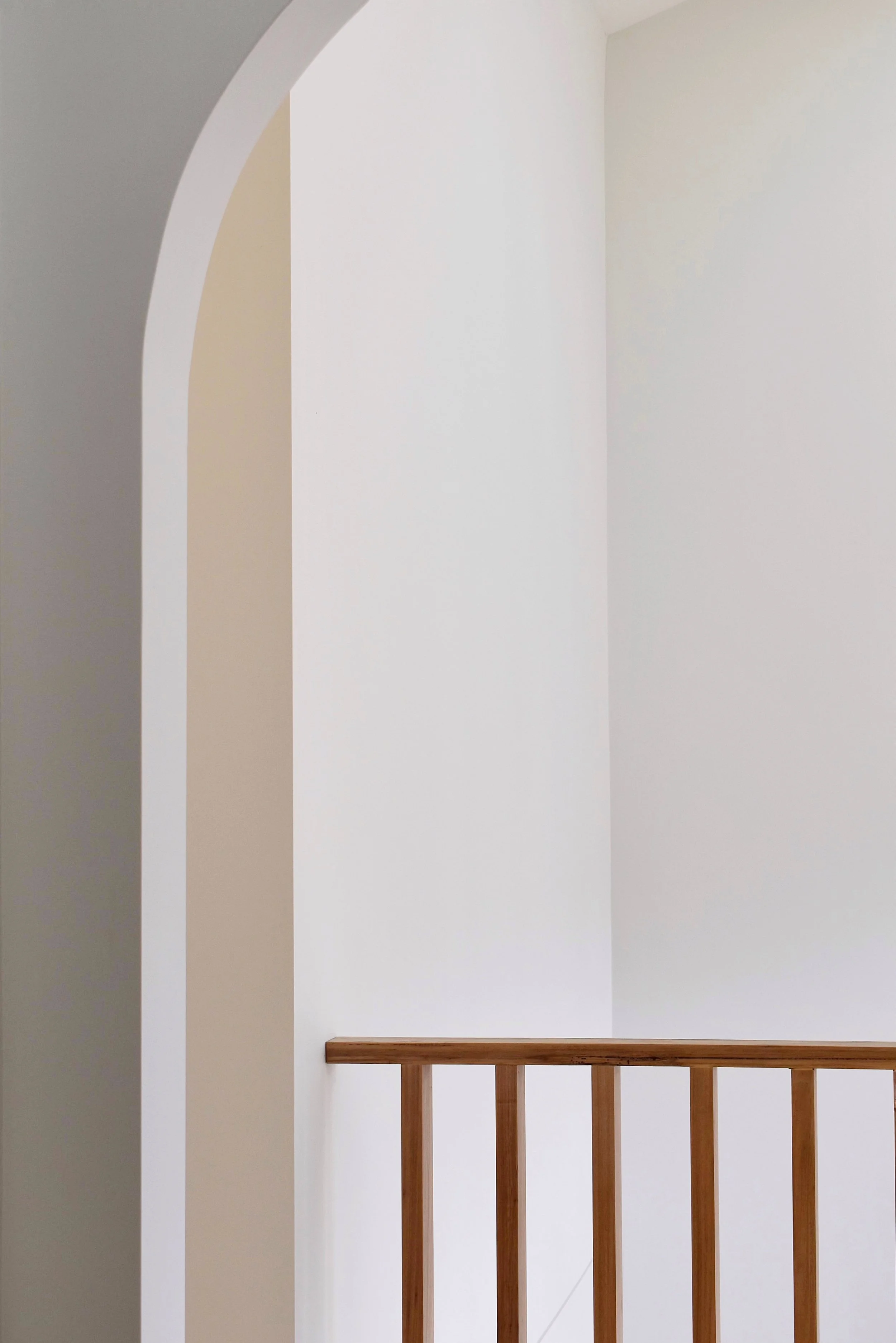 Interior view of a staircase landing with white walls, archways, and wooden handrails.