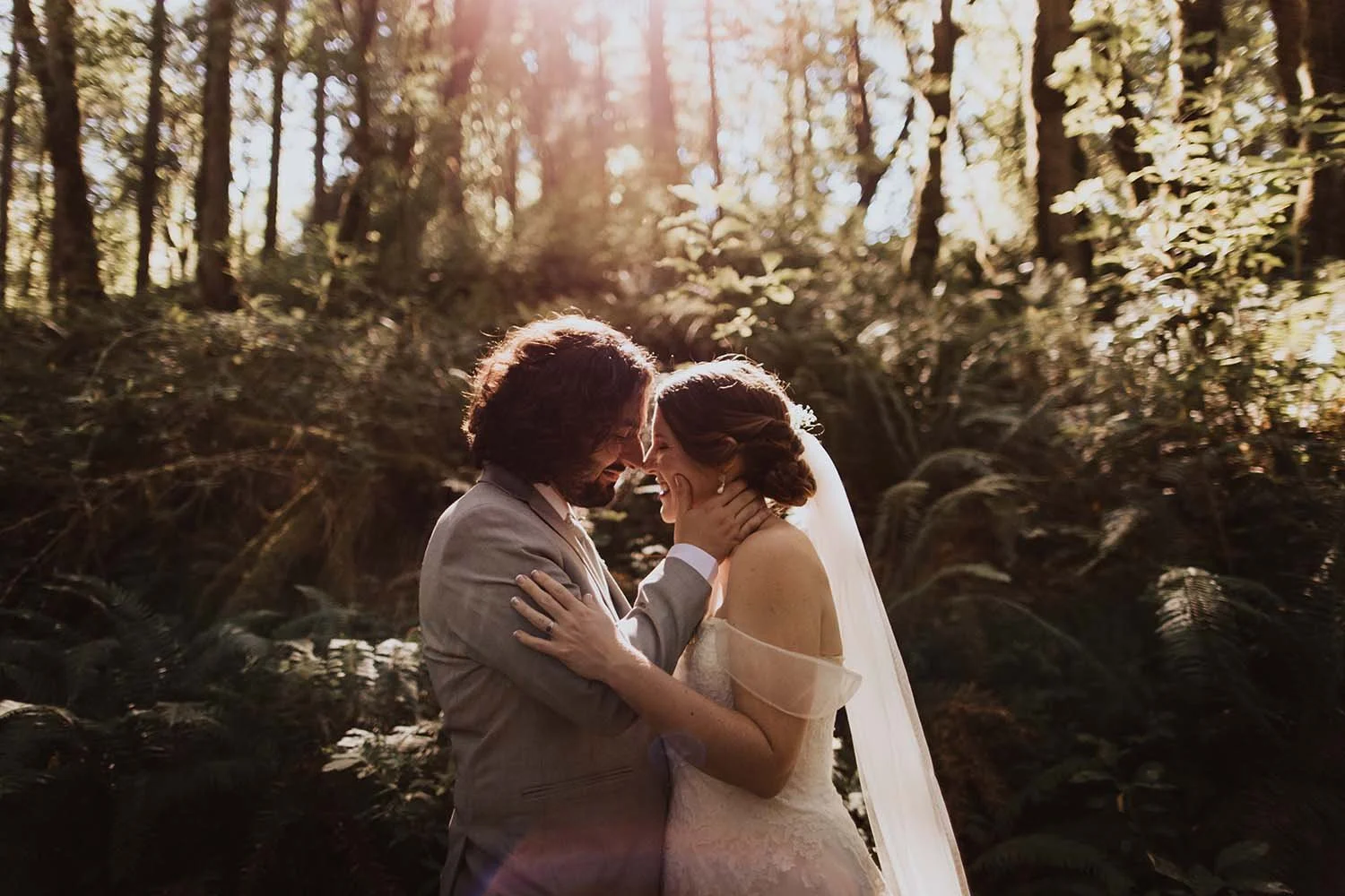 A bride and groom embrace each other in a forest with the sun shining through the trees.