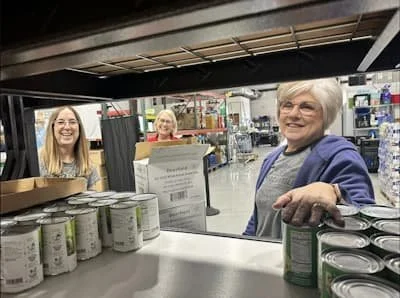 Three volunteers happily stocking shelves with food items