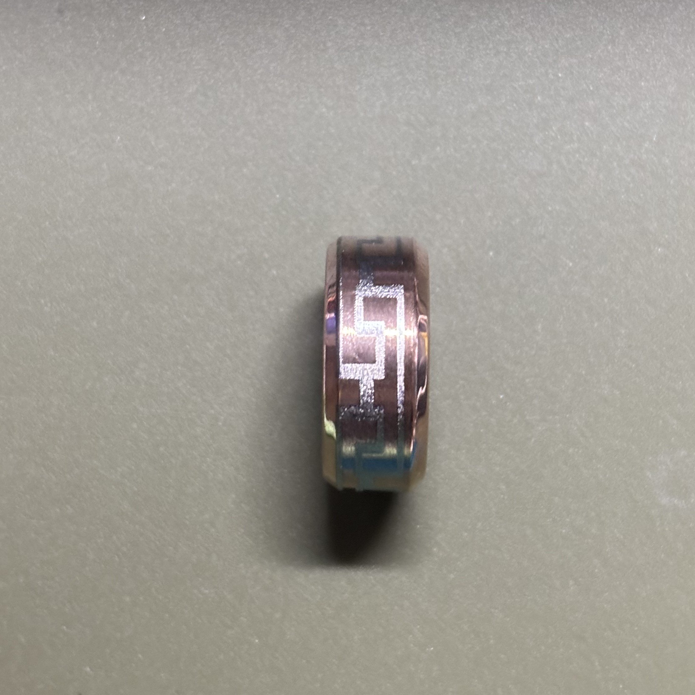 Close-up of a metallic ring with engraved geometric patterns on a plain gray surface.