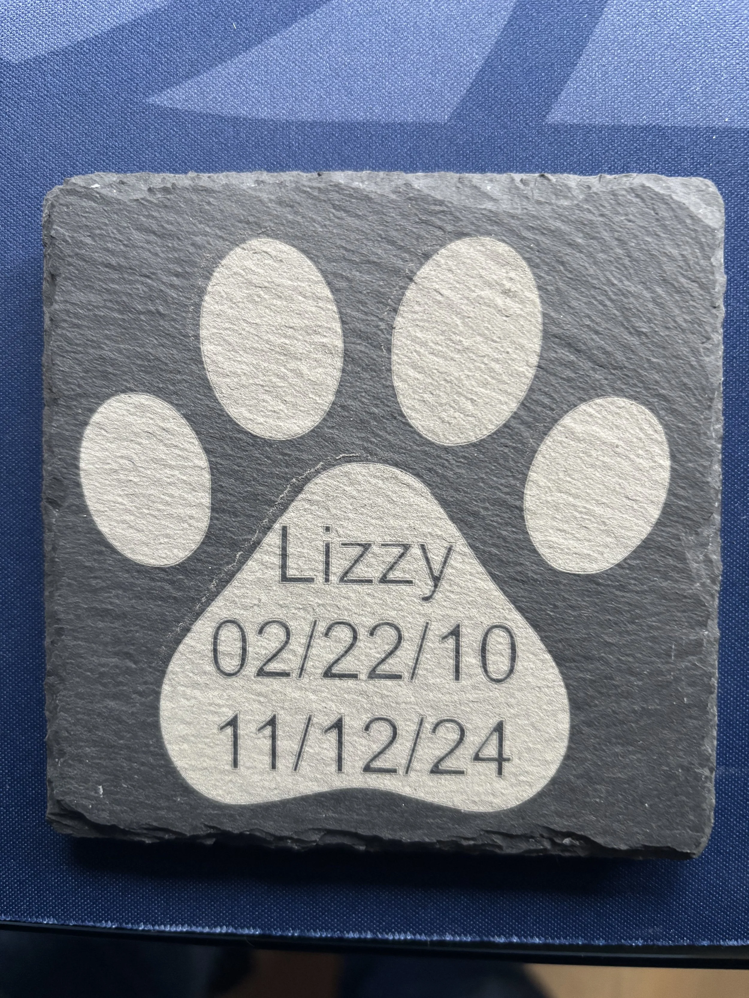 A gray stone with a paw print design and the name Lizzy, birth date 02/22/10, and death date 11/12/24 engraved on it.