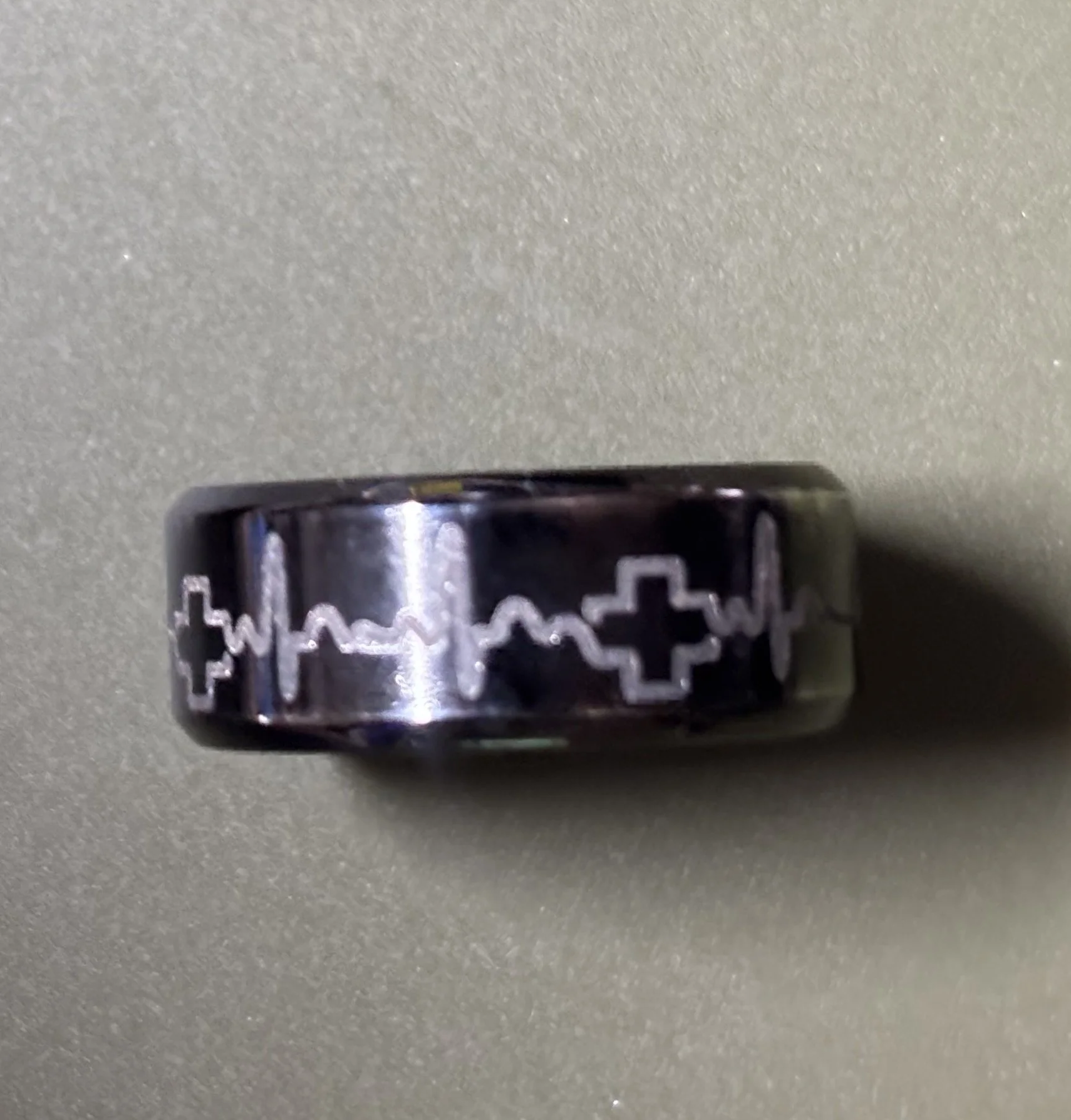 A black ring with white tattoo-style crosses and a heartbeat line pattern.