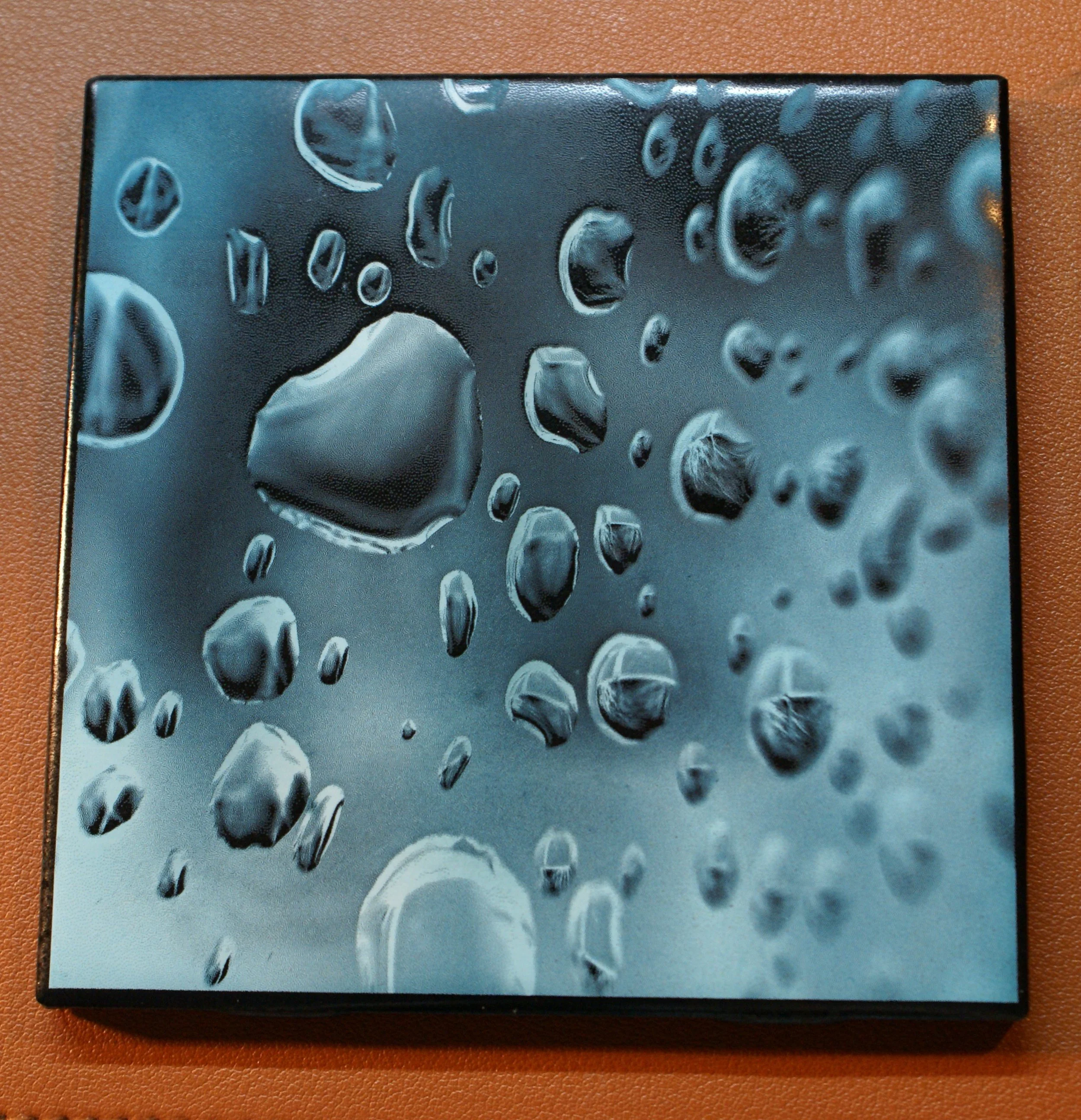 Close-up of water droplets on a reflective surface with a textured background.