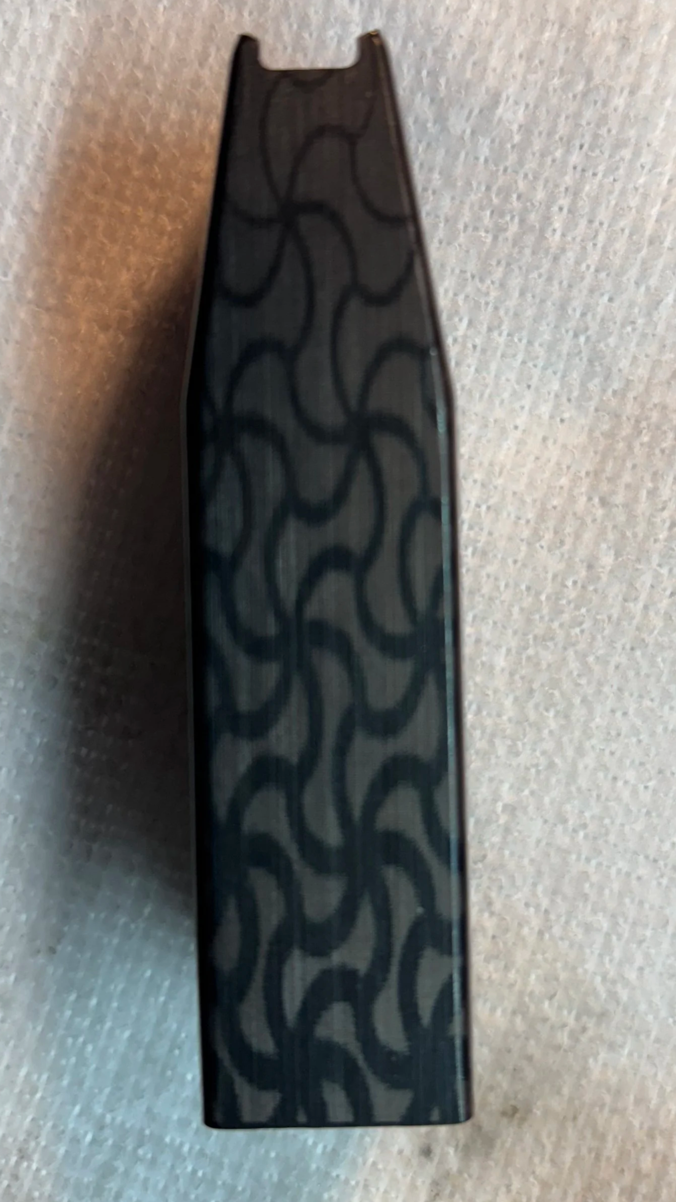 Close-up of a black object with wavy pattern on its surface, likely made of plastic or metal, placed on a light-colored textured surface.
