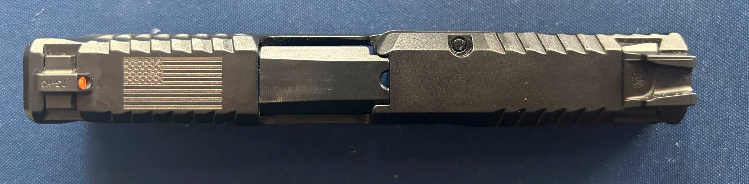 Top view of a black semi-automatic handgun with textured grip on a dark blue surface.