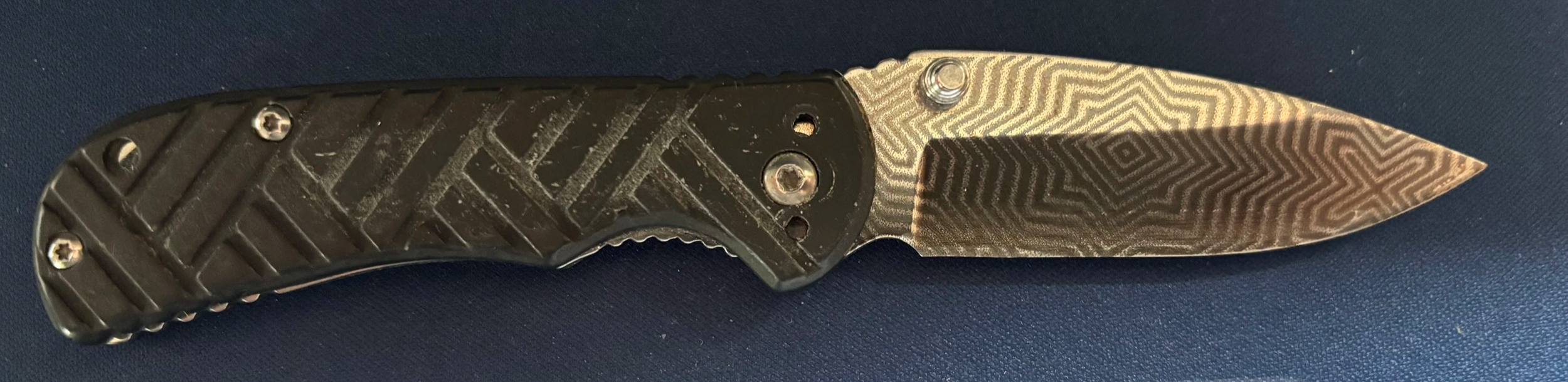 A folding pocket knife with a textured black handle and a patterned metal blade.