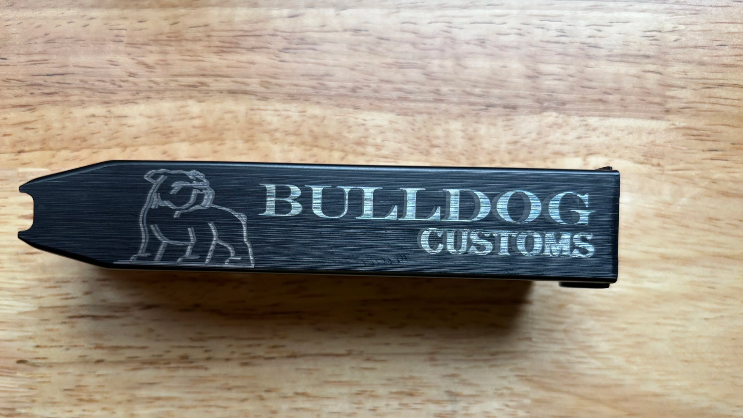 A black item with a bulldog logo and the words "BULLDOG CUSTOMS" engraved on it, placed on a wooden surface.
