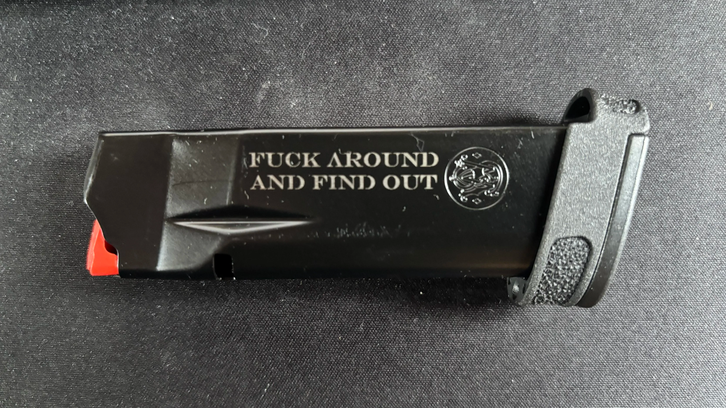 A black object with the words 'FUCK AROUND AND FIND OUT' printed in white, placed on a black surface.