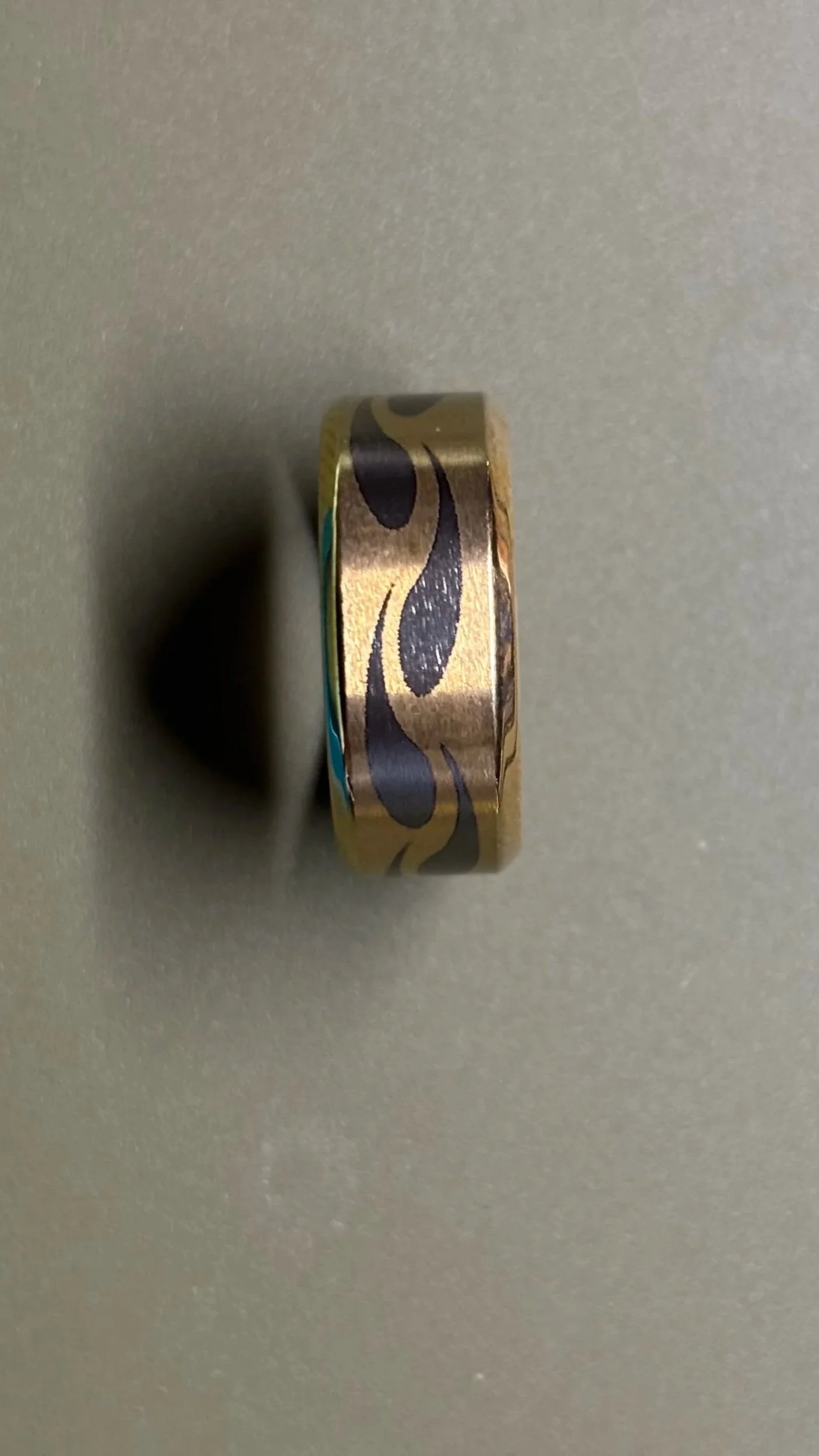 Close-up of a decorative ring with a black and gold pattern on a grey surface.