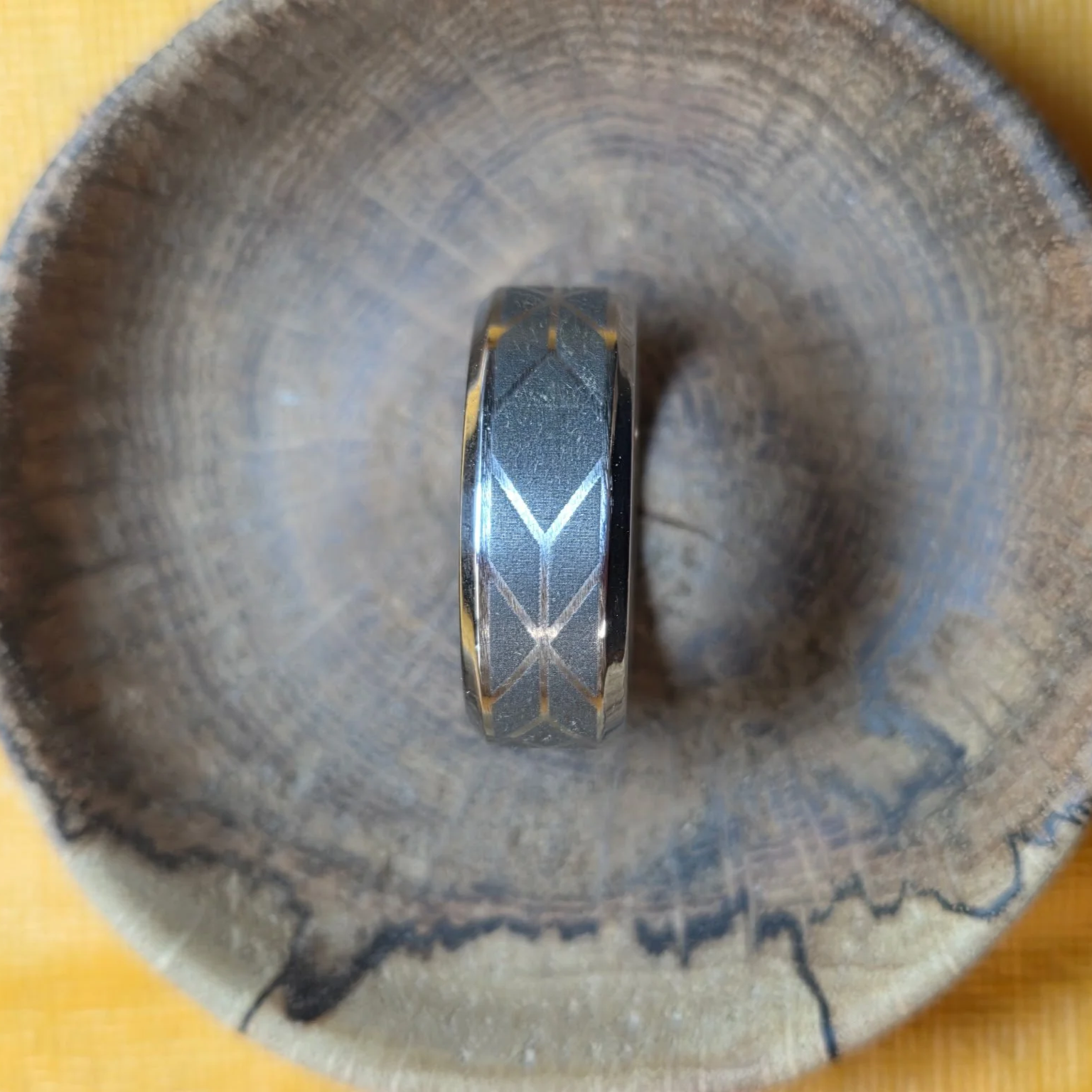 A silver ring with geometric patterns placed inside a wooden cup or container.