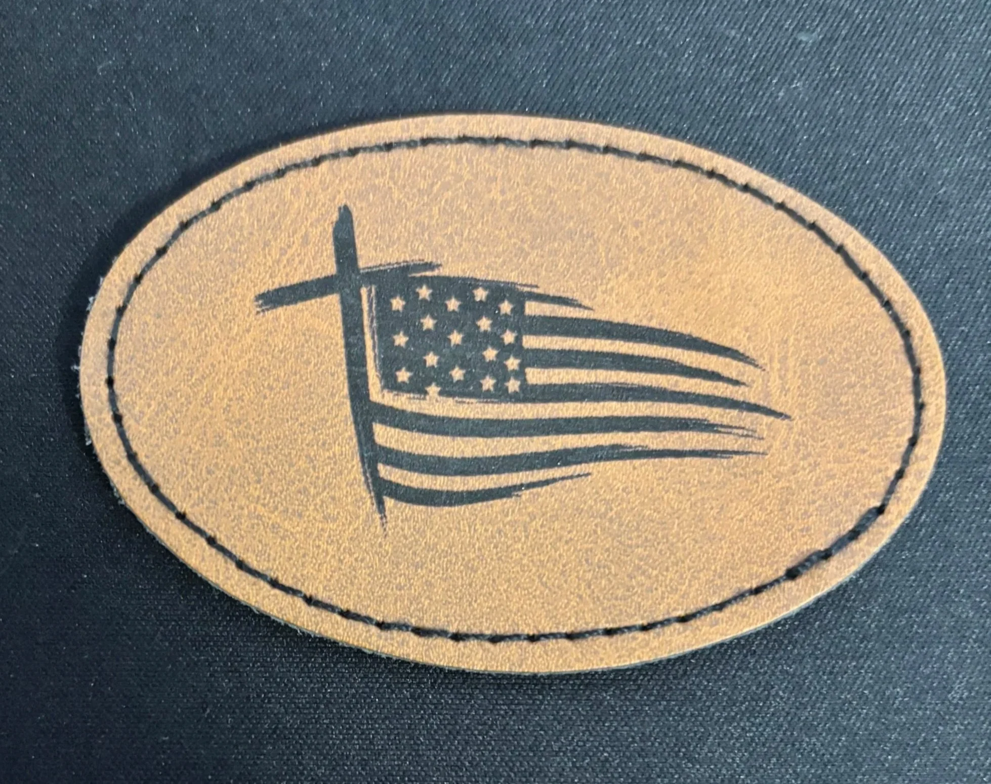 A patch with an American flag and a cross, on a black fabric background.