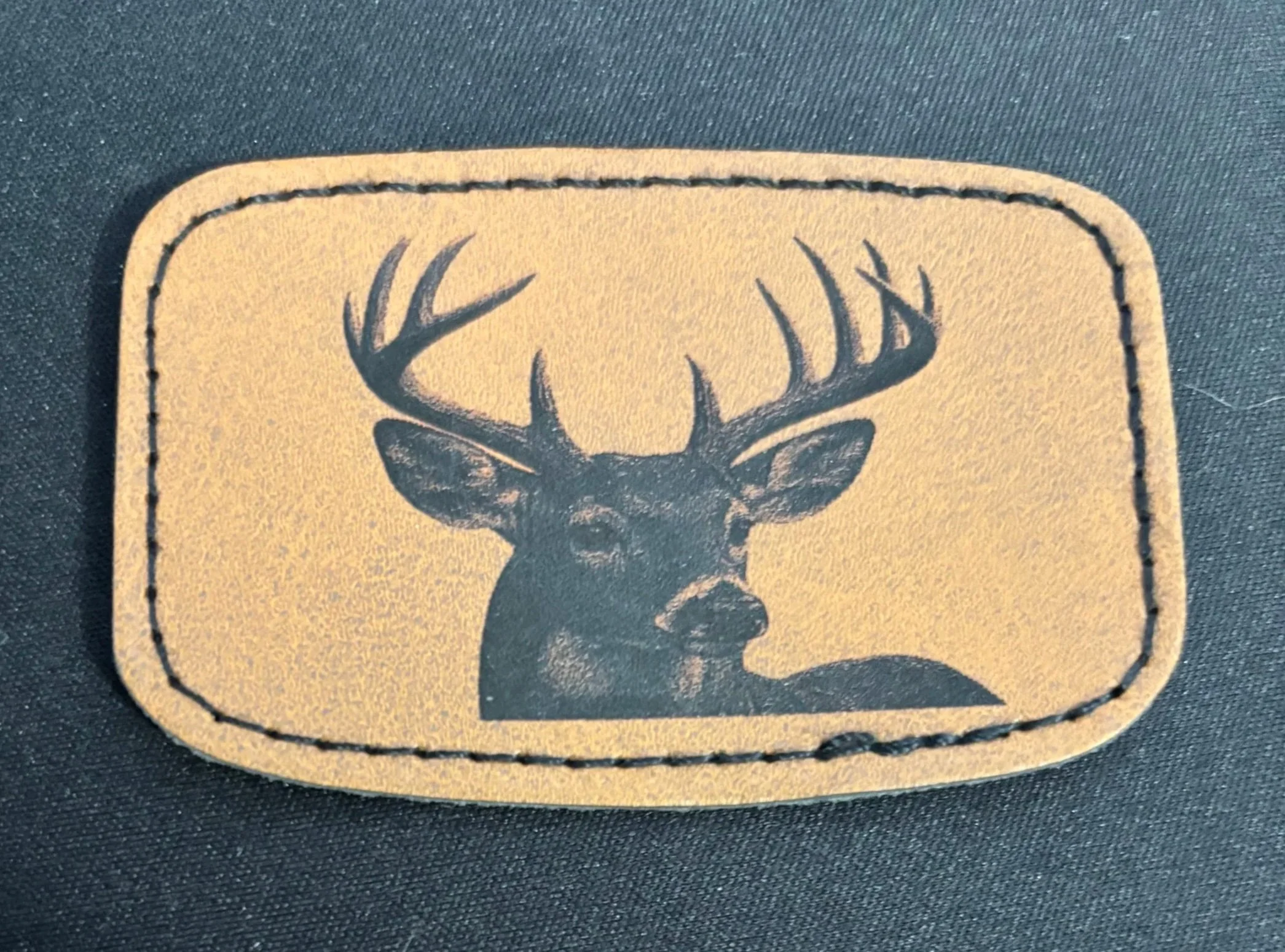 Leather patch with a black silhouette of a deer with large antlers on a tan background, stitched border.