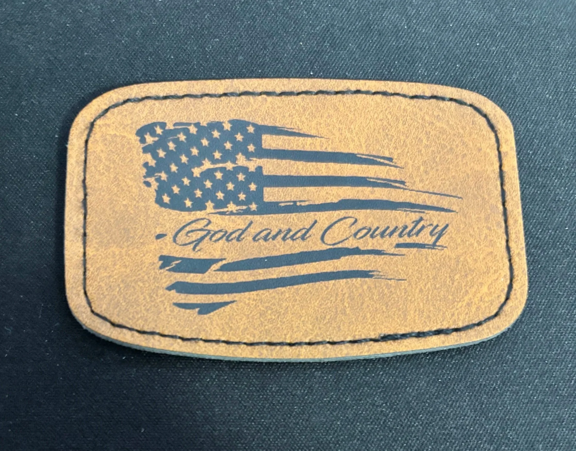 Leather patch with an American flag and the text 'God and Country' on a dark fabric background.