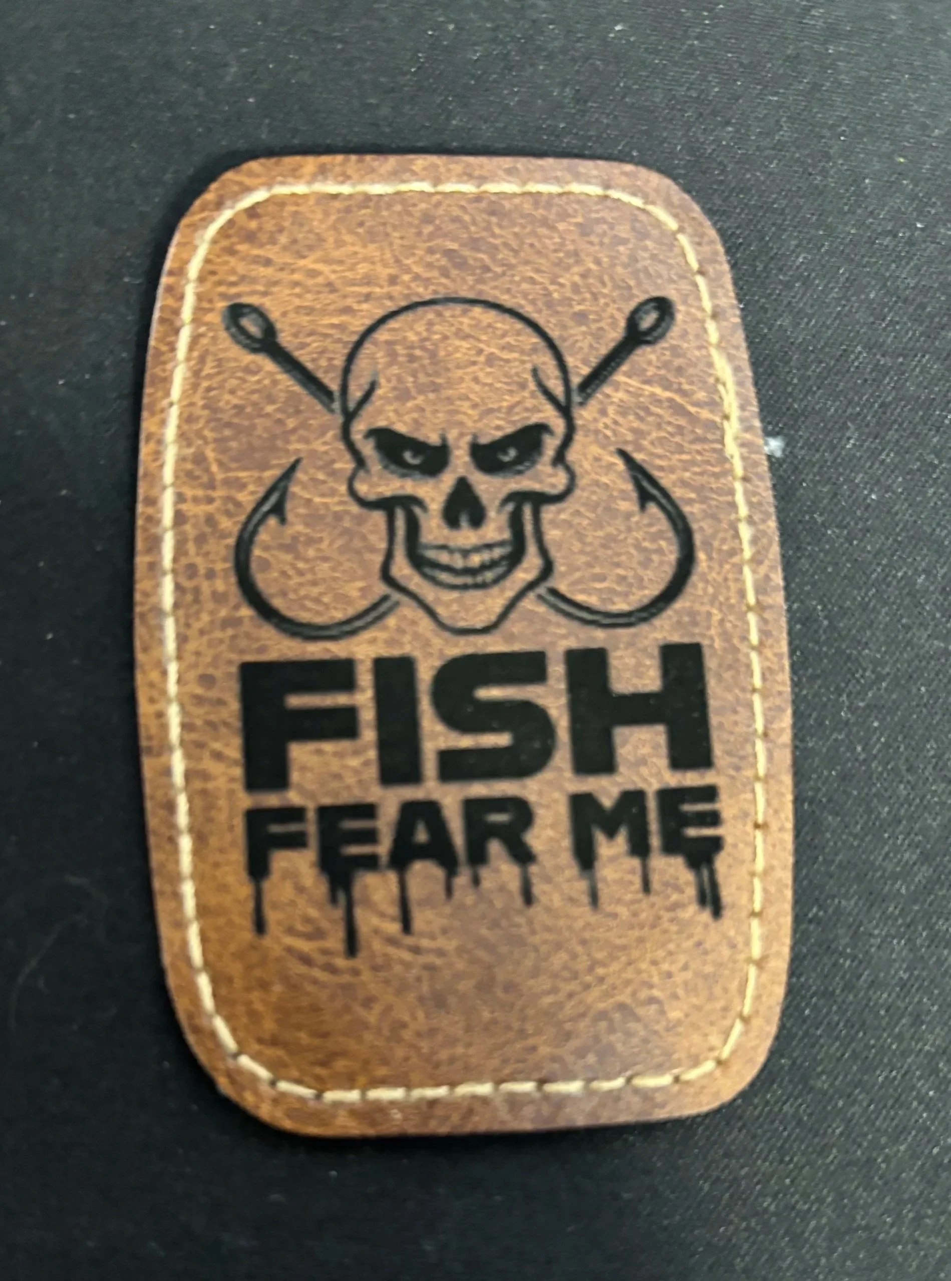 Leather patch with a skull illustration, crossed fishing hooks, and the text "FISH FEAR ME".
