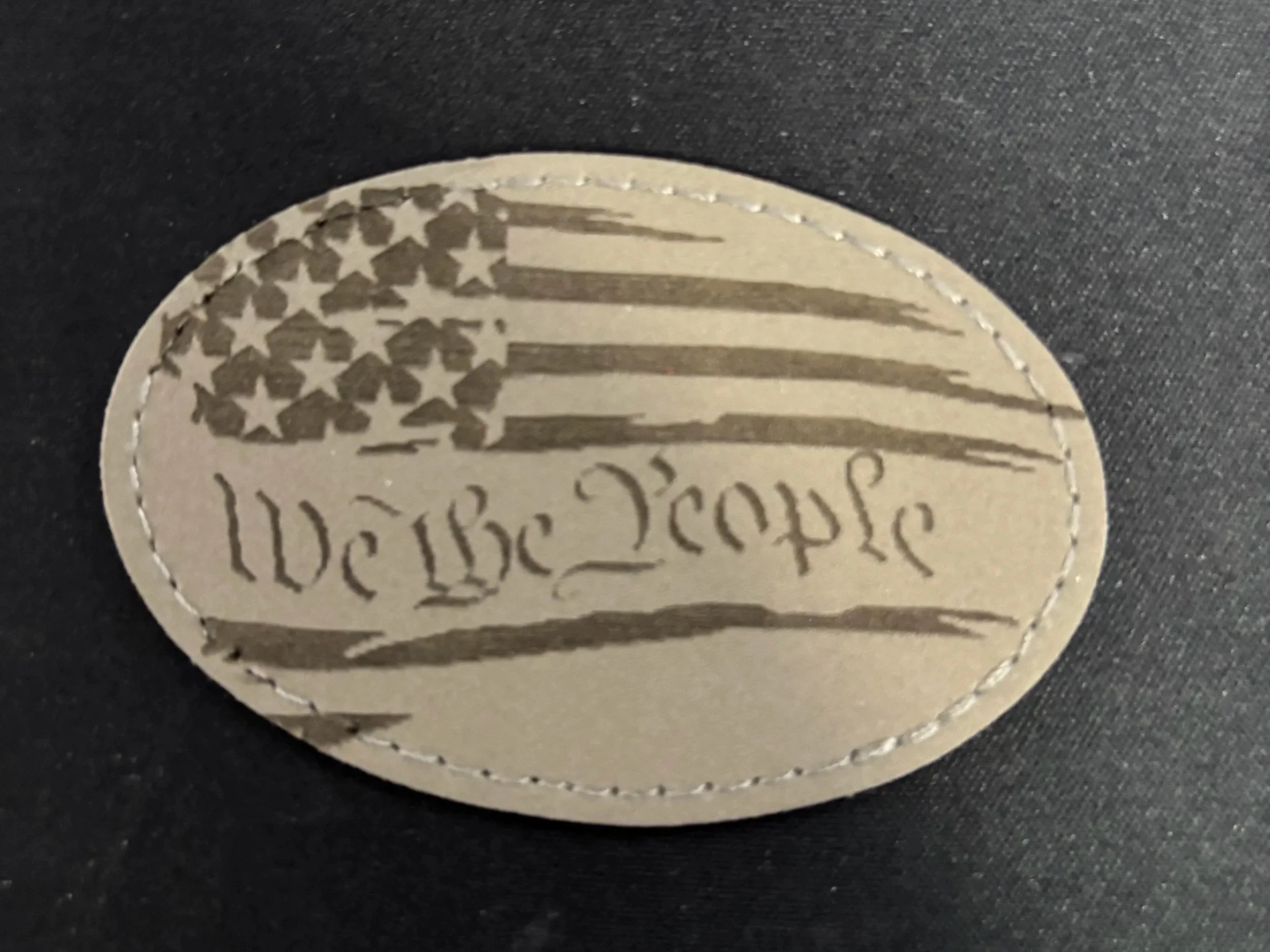A circular patch with a distressed American flag design and the words 'We The People' written below the flag.