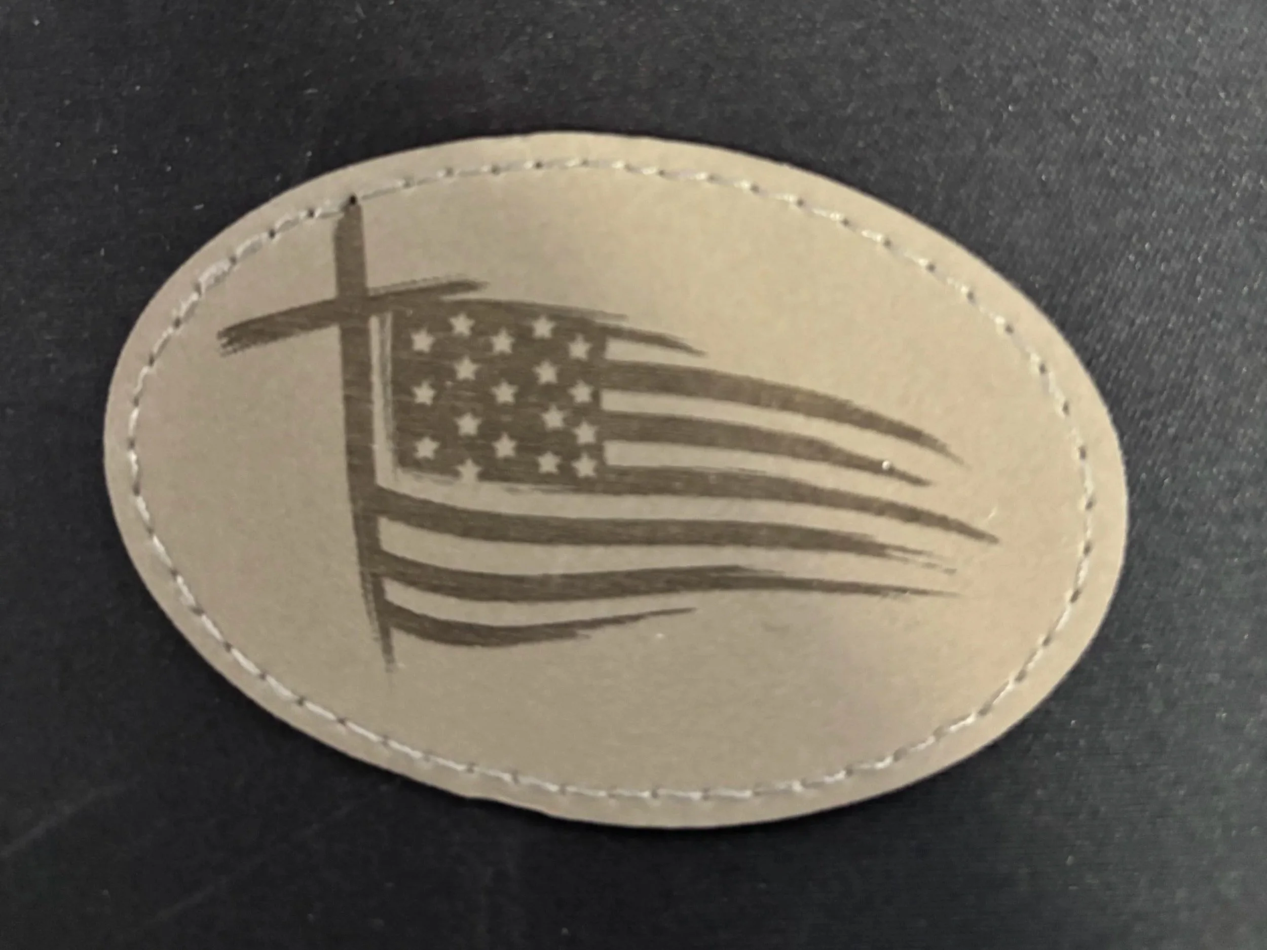 Oval patch with a stylized American flag design in black and gray.