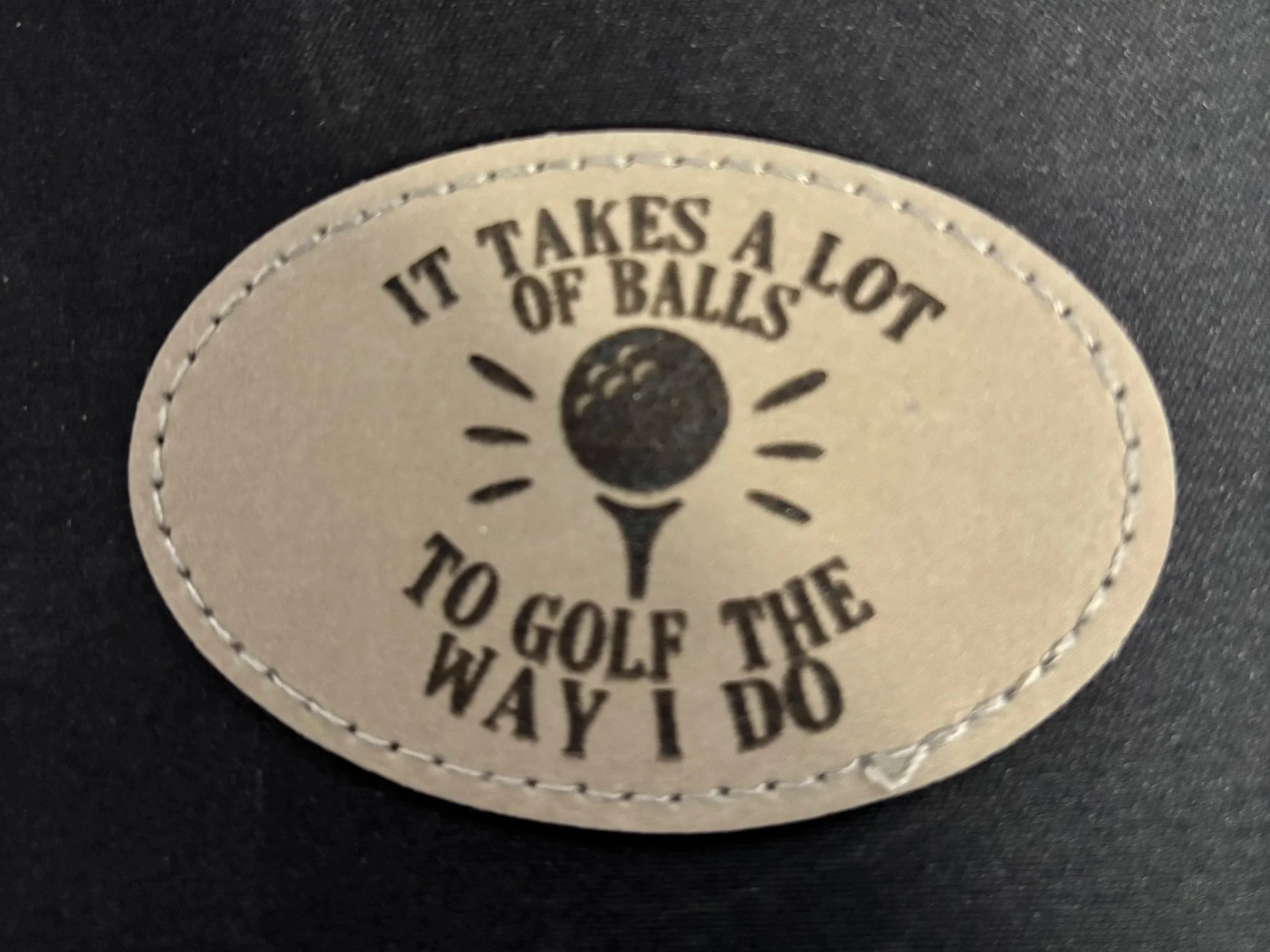 A circular patch with a golf ball illustration in the center, surrounded by the text "It takes a lot of balls to golf the way I do".