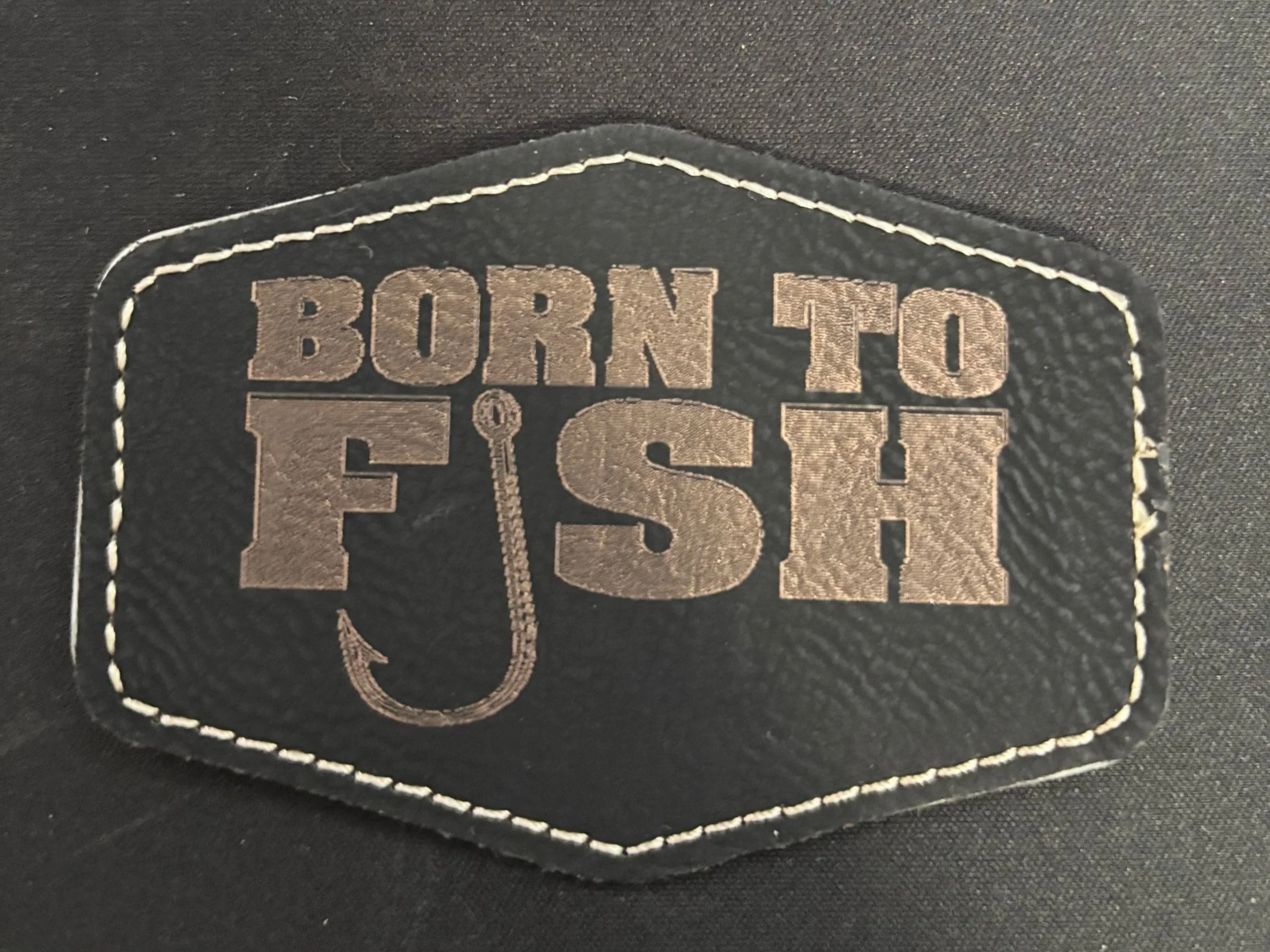 Black fabric patch with the words 'BORN TO FISH' and a fishing hook graphic.