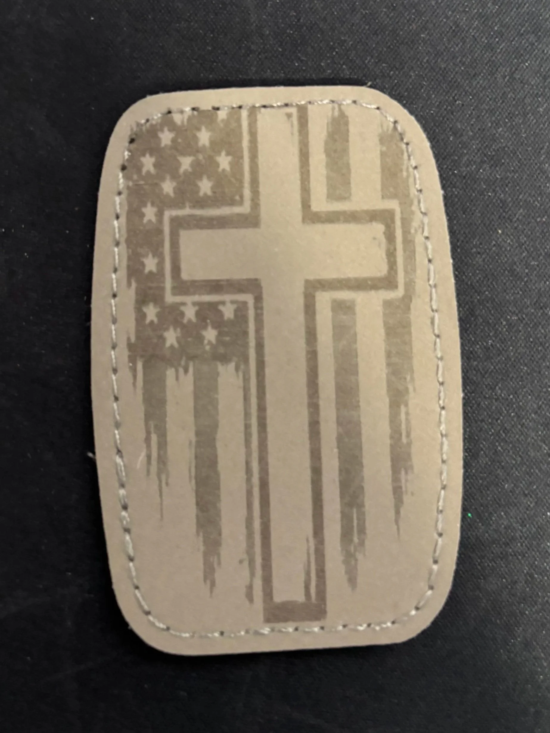A fabric patch with a design of a cross over an American flag with distressed and stylized appearance.